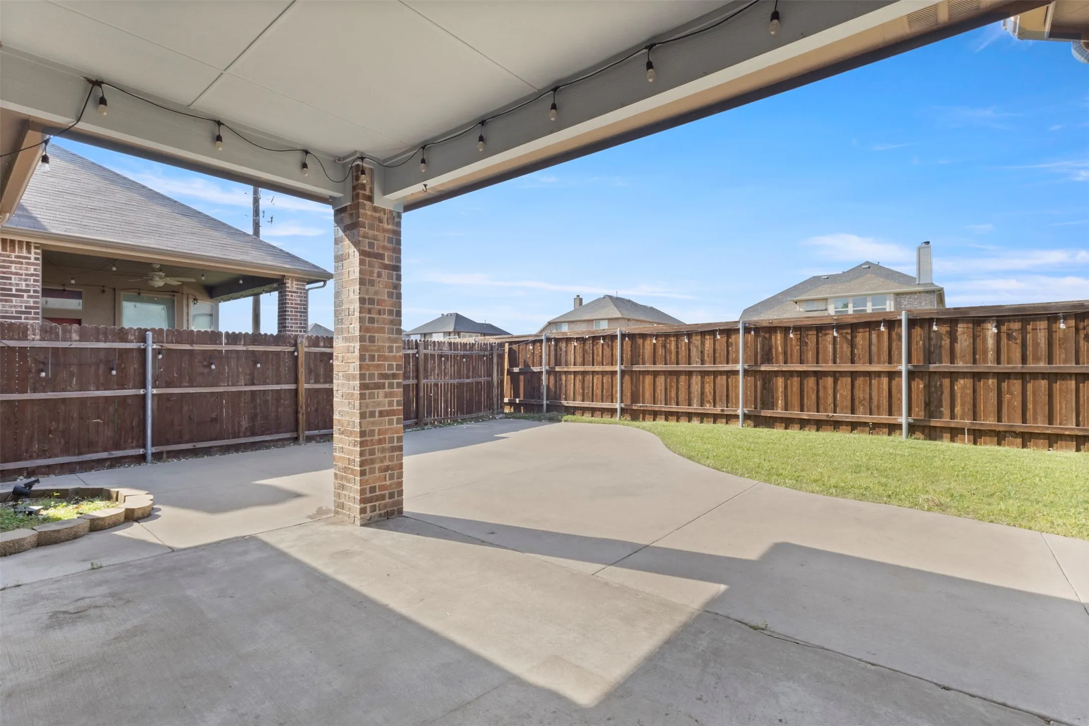 The property features a covered patio with string lights, a brick support column, and concrete paving