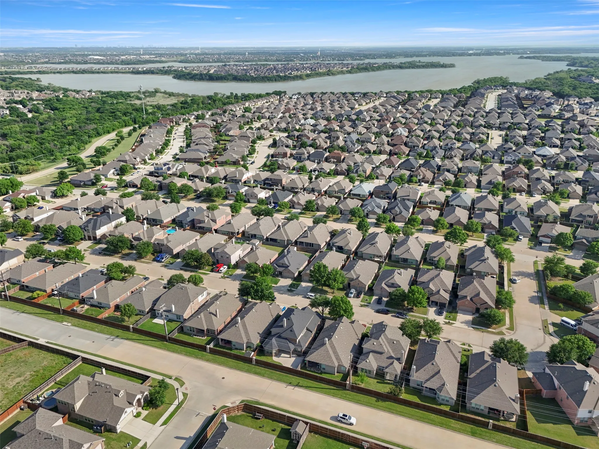 An aerial view showcasing the established neighborhood with a mix of residential properties, green spaces, and a nearby body of water under a clear sky