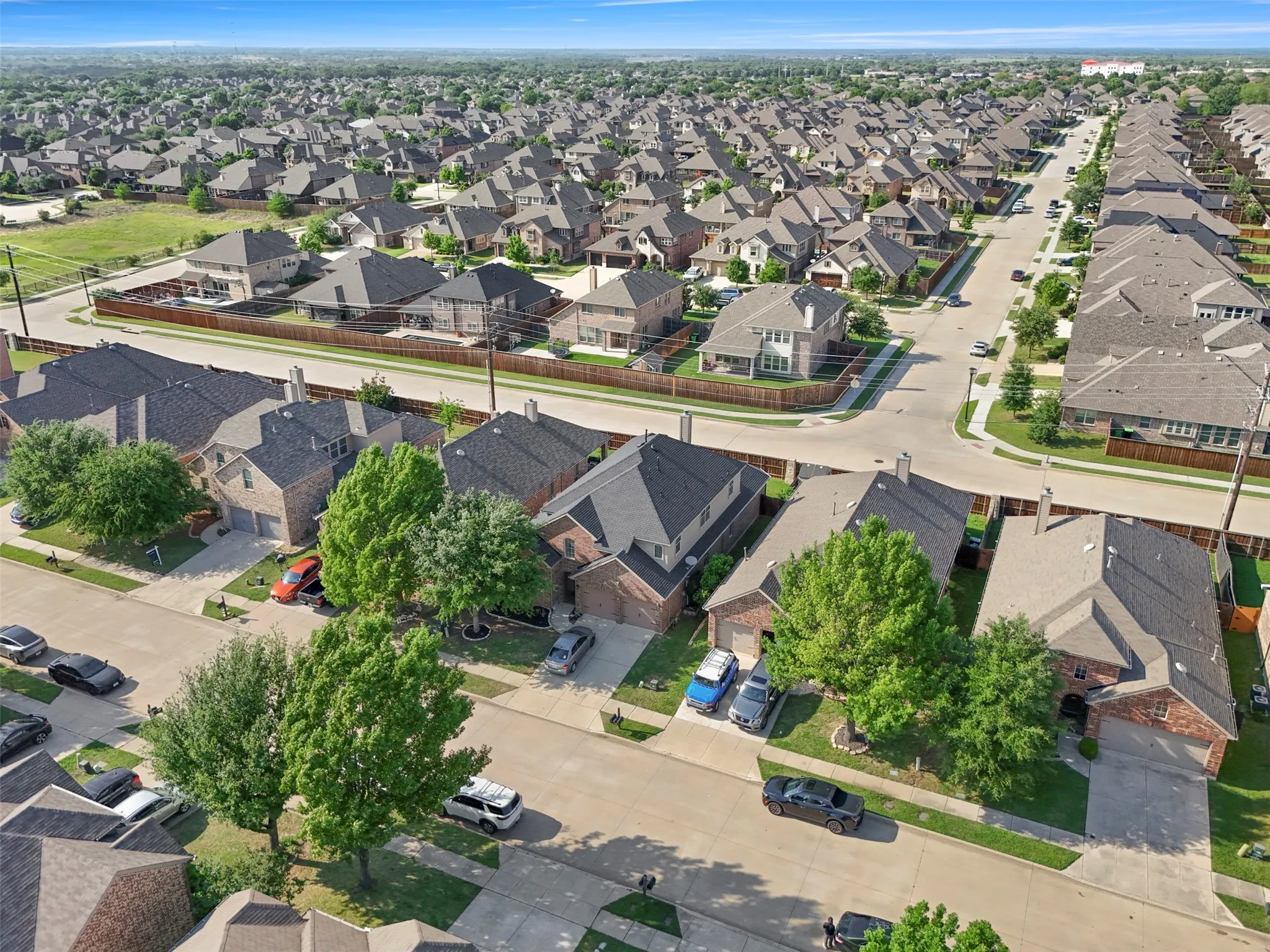 This aerial view showcases the property within a well-established neighbourhood featuring numerous homes with brick exteriors and pitched roofs, surrounded by mature trees and paved streets