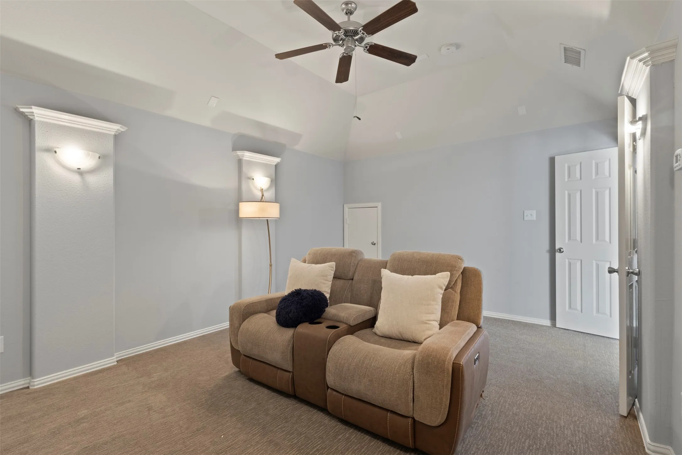 This room features a vaulted ceiling with a ceiling fan, sconce lighting, and carpeted flooring