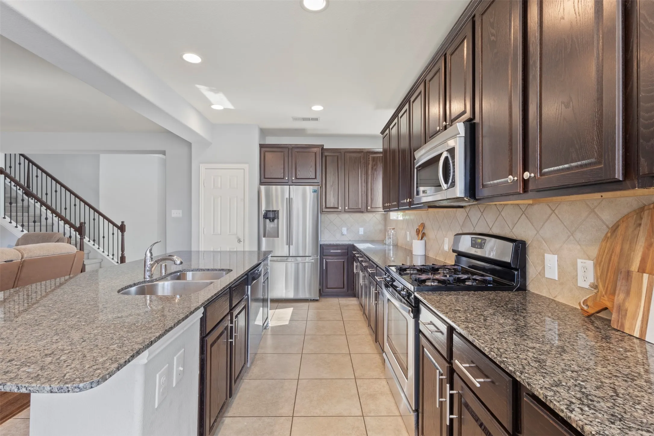 The kitchen features granite countertops, dark wood cabinetry, and stainless steel appliances including a refrigerator, microwave, and gas range