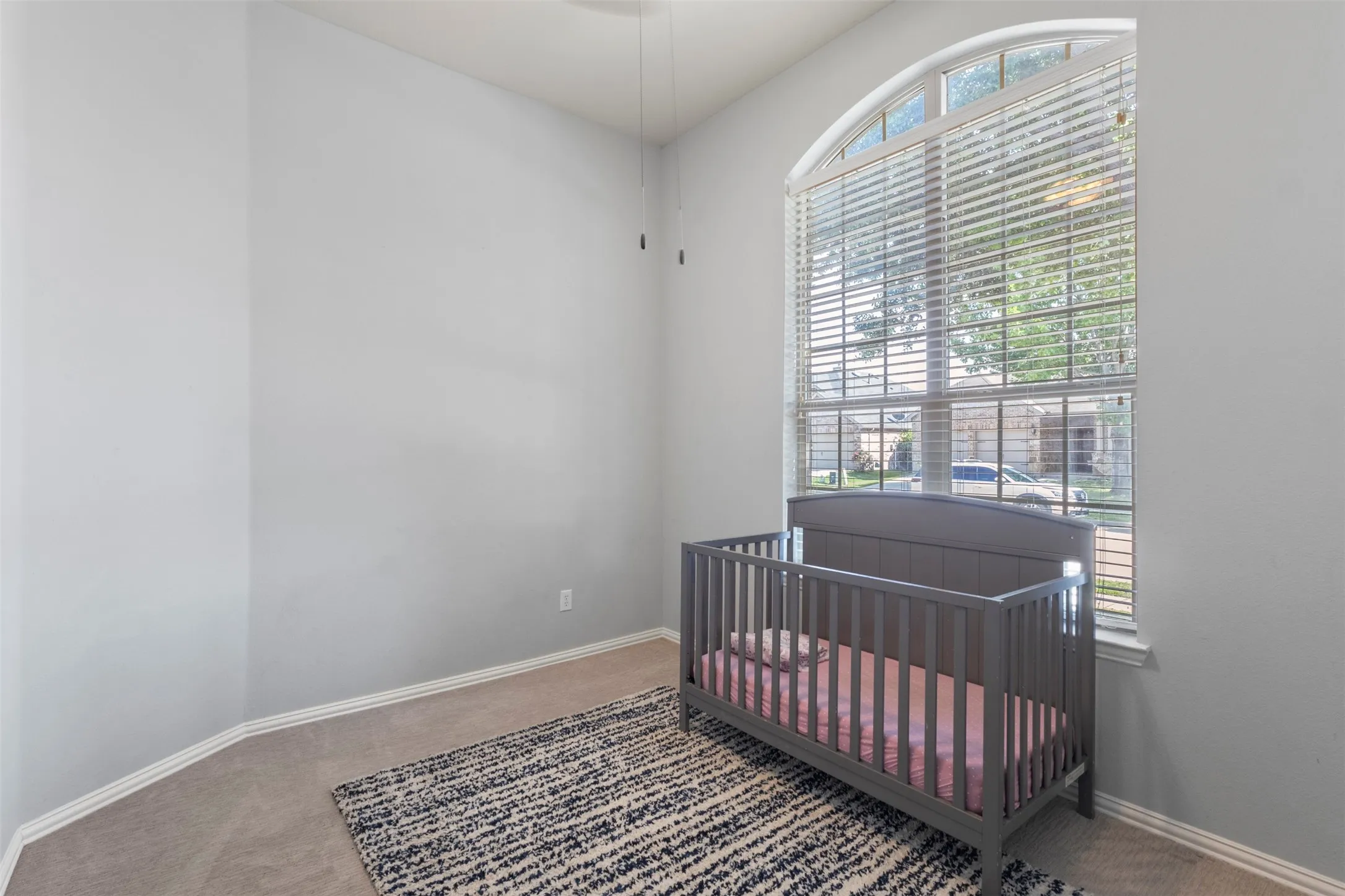This room features neutral-toned walls, carpeting, and an arched window with blinds