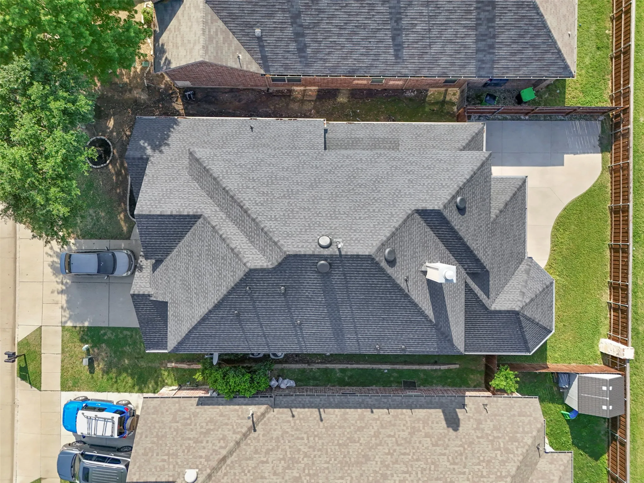 Aerial view showcasing the property's gray shingled roof, a concrete driveway, and a fenced yard with green lawn