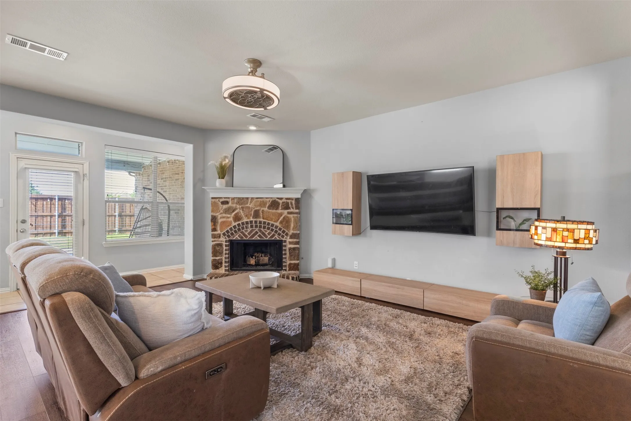 The living room features a stone fireplace with a white mantel, a ceiling fan, and hardwood flooring