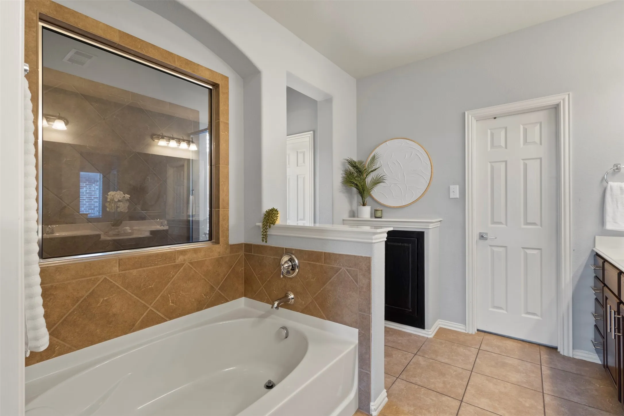 Bathroom featuring a built-in bathtub with a tile surround, a large window, and tile flooring