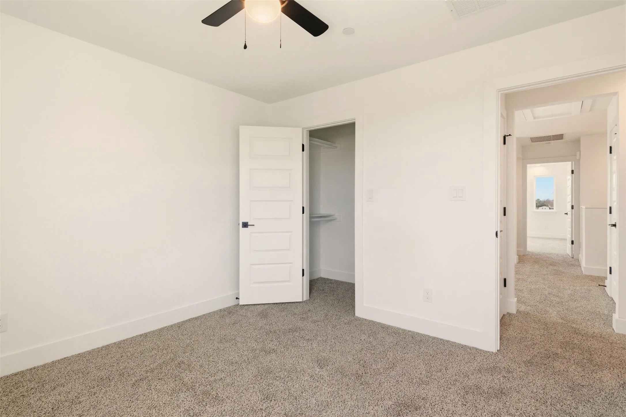 This room features neutral-toned carpeting, a ceiling fan with integrated lighting, and a white paneled door leading to a closet with shelving