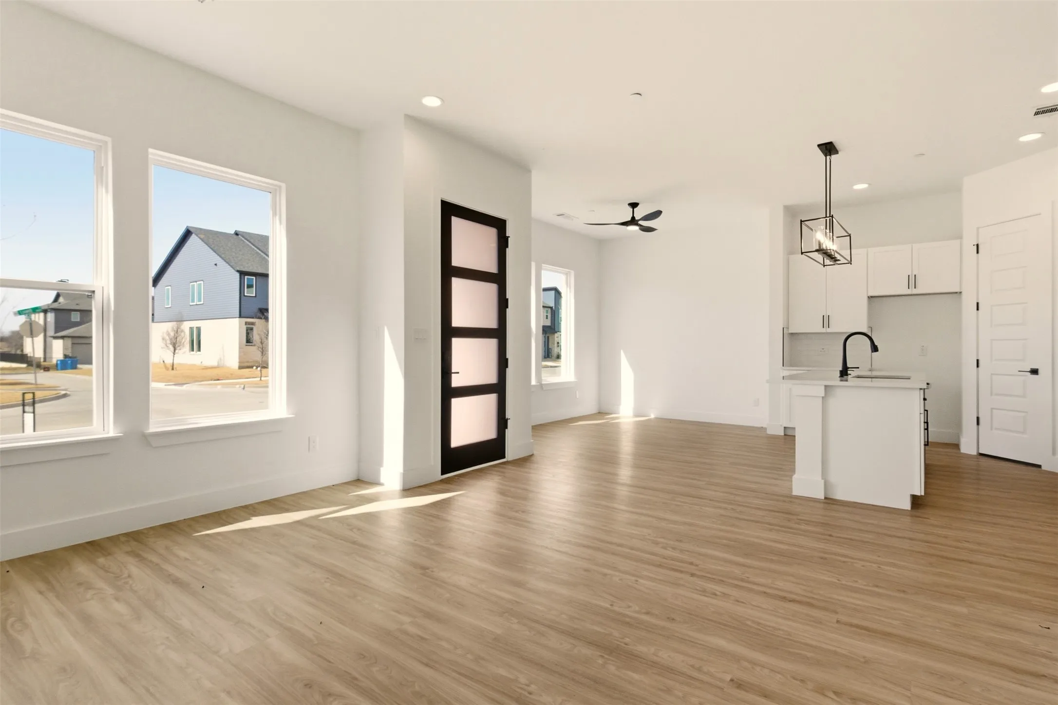 Open concept living space featuring light wood-look flooring, large windows, recessed lighting, and a kitchen area with white cabinetry and an island