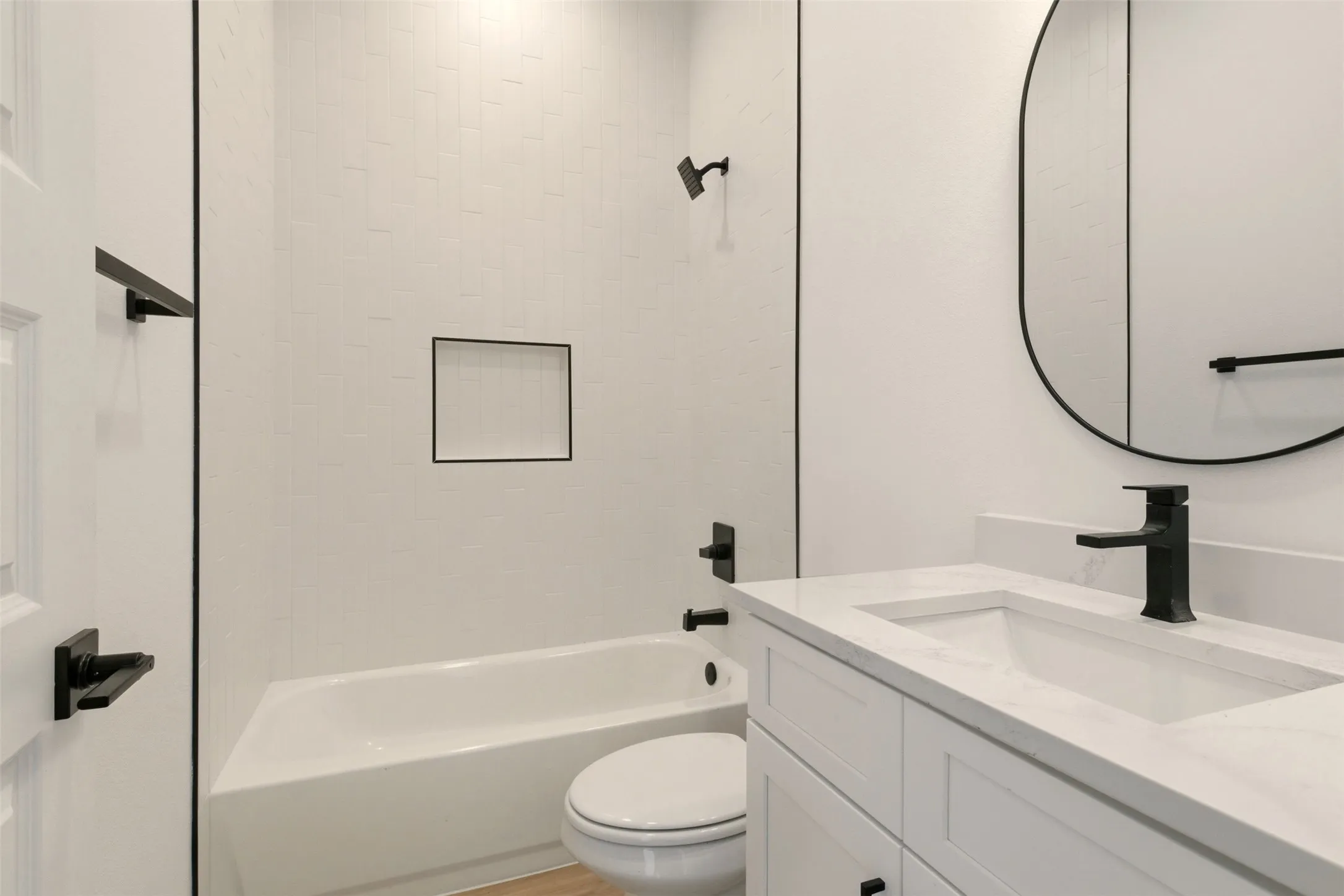 Bathroom featuring a white vanity with an integrated sink, black faucet, and an oval mirror