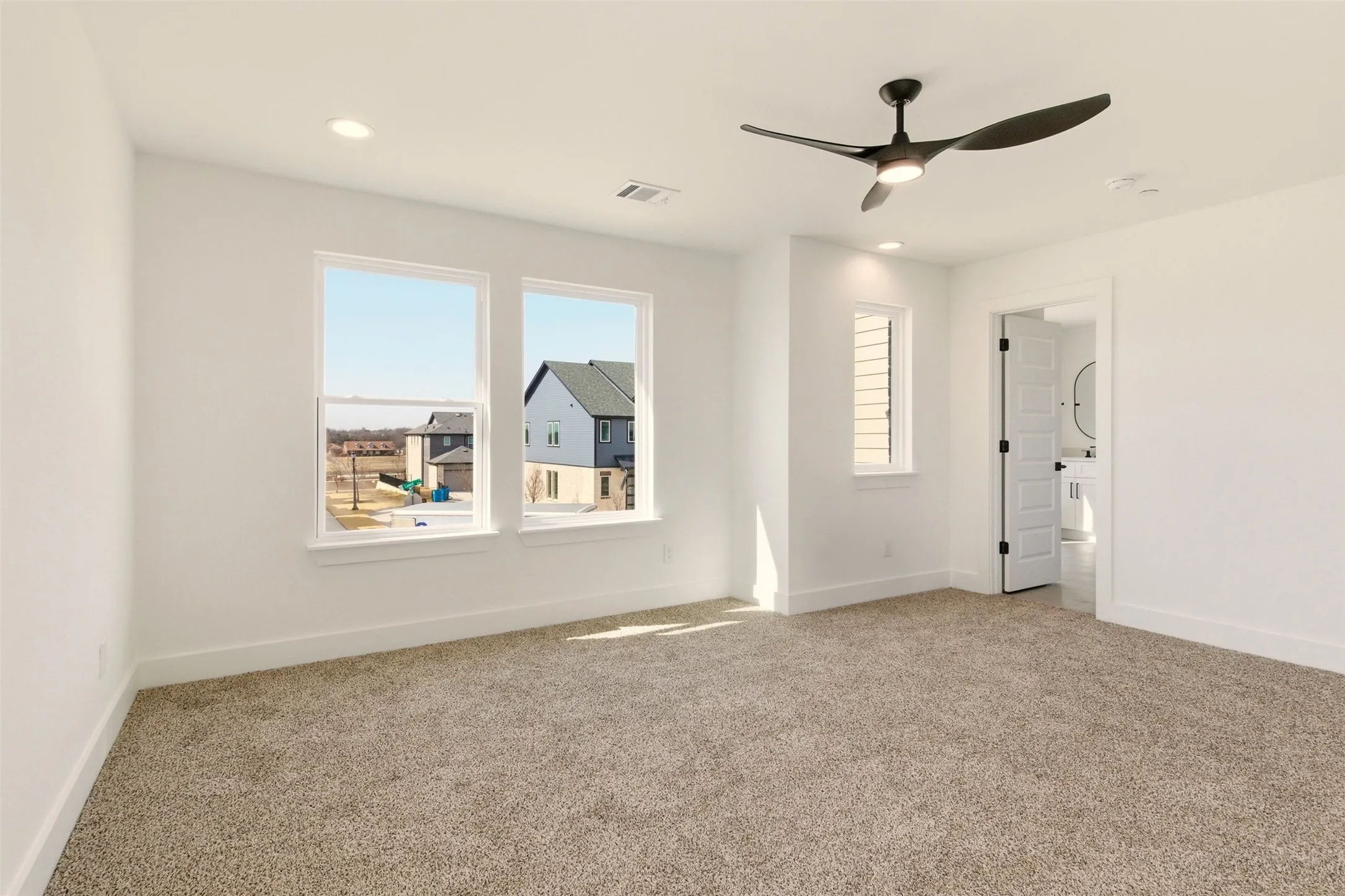 This spacious room features neutral-toned carpet, a contemporary ceiling fan, and recessed lighting