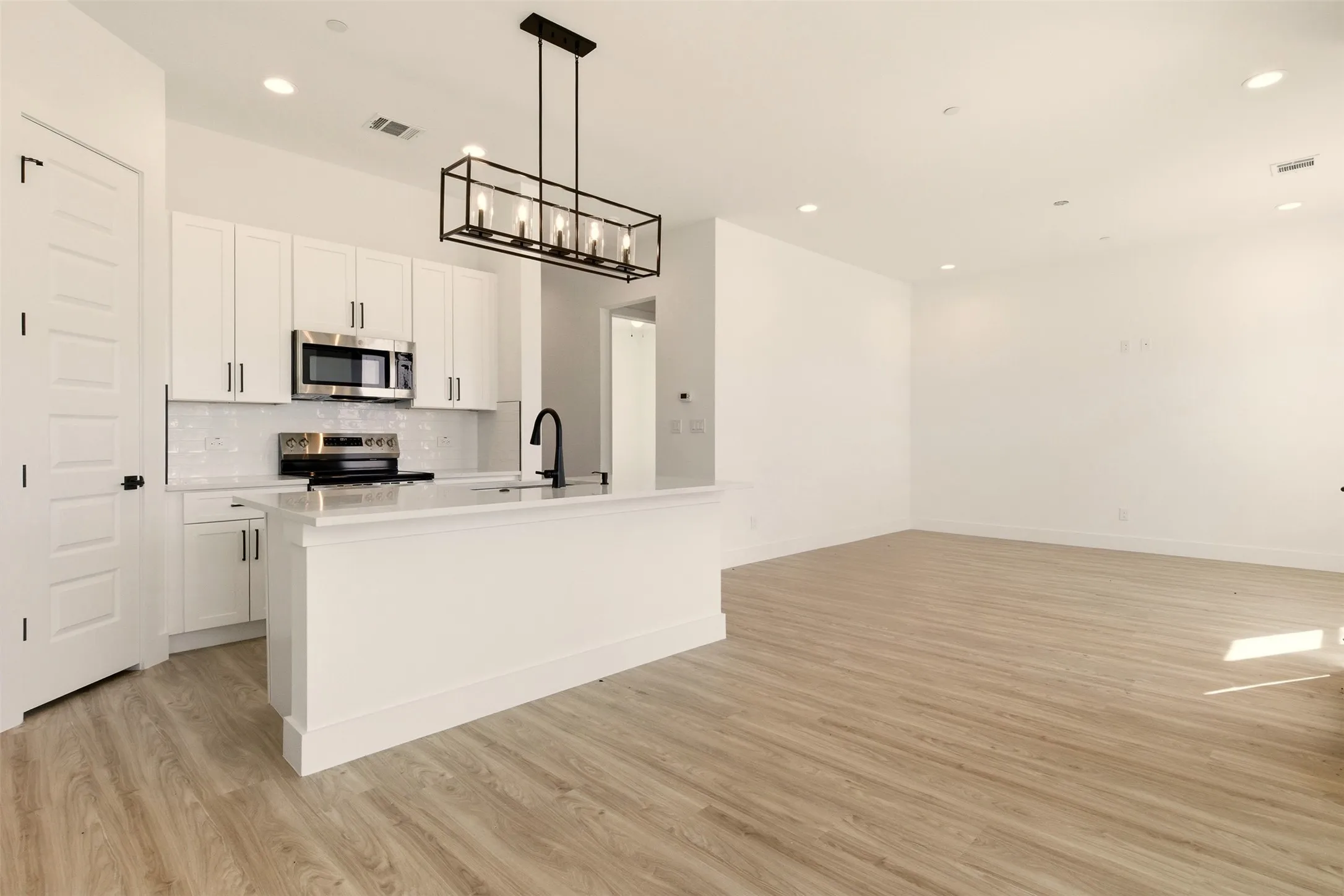 The property features an open-concept living space with light wood-style flooring, a kitchen island with a white countertop, and a kitchen equipped with stainless steel appliances
