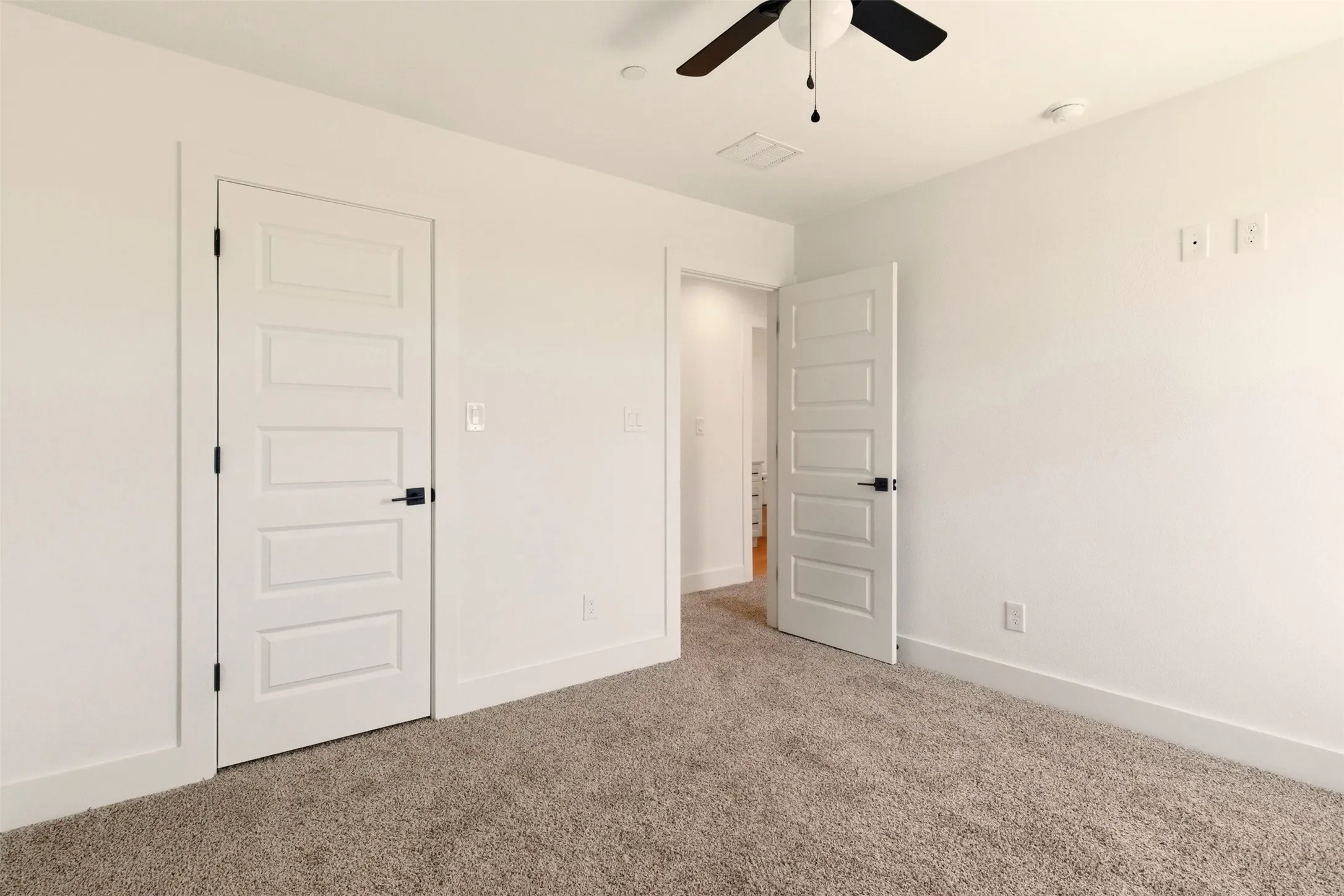 Spacious room featuring neutral carpeting, white walls, and a ceiling fan