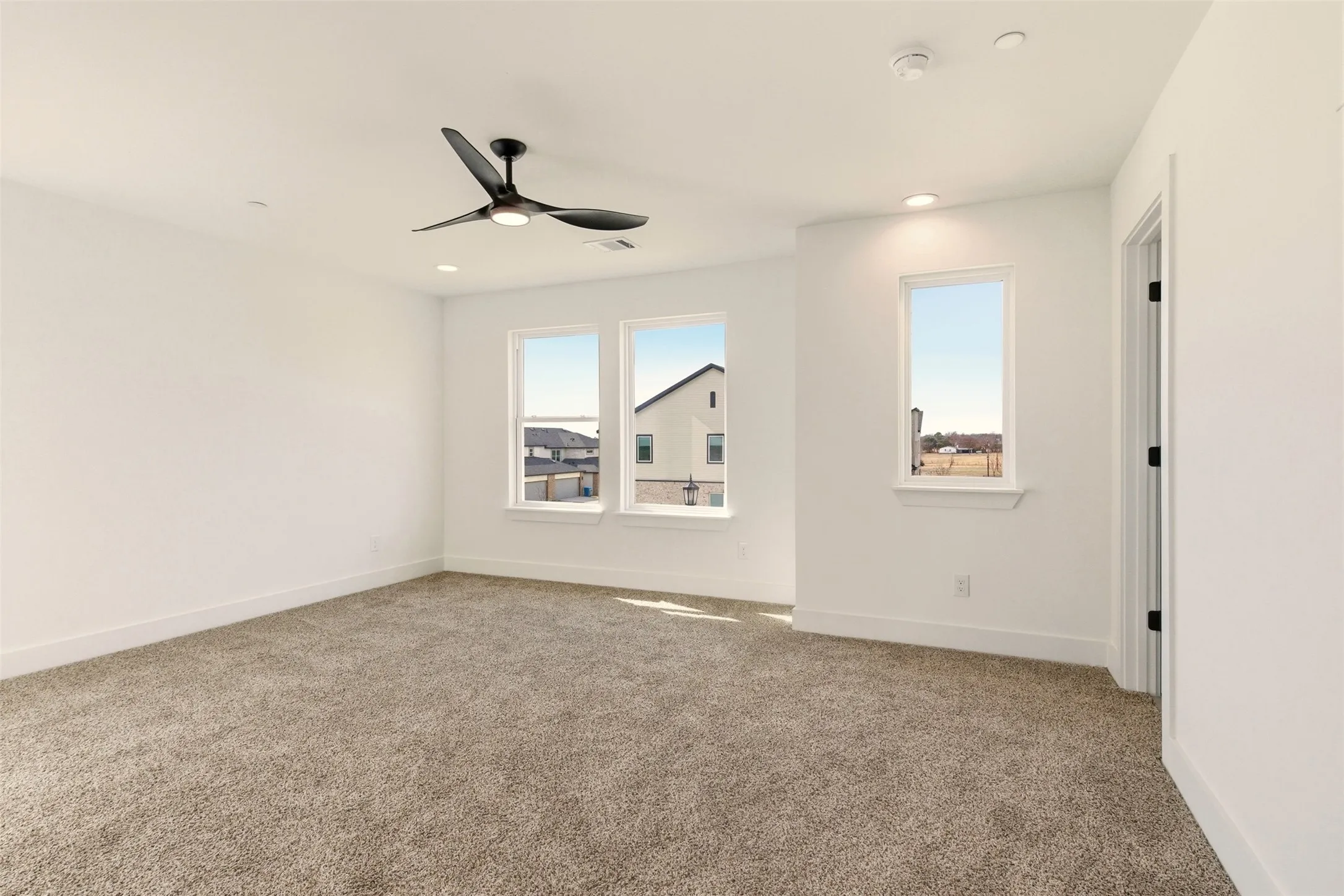 Spacious room featuring carpeted flooring, white walls, a ceiling fan, and multiple windows providing ample natural light
