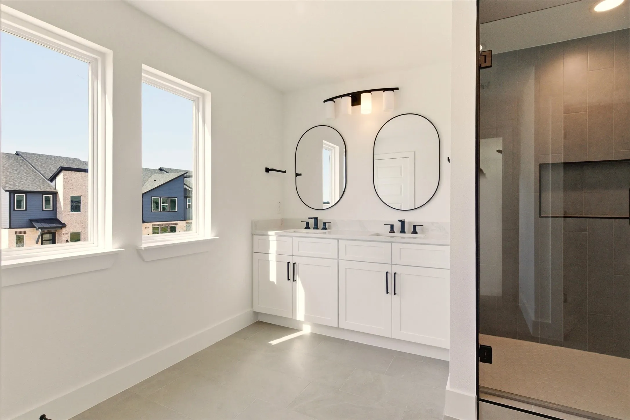 This bathroom features a double vanity with white cabinetry, black hardware, and two oval mirrors