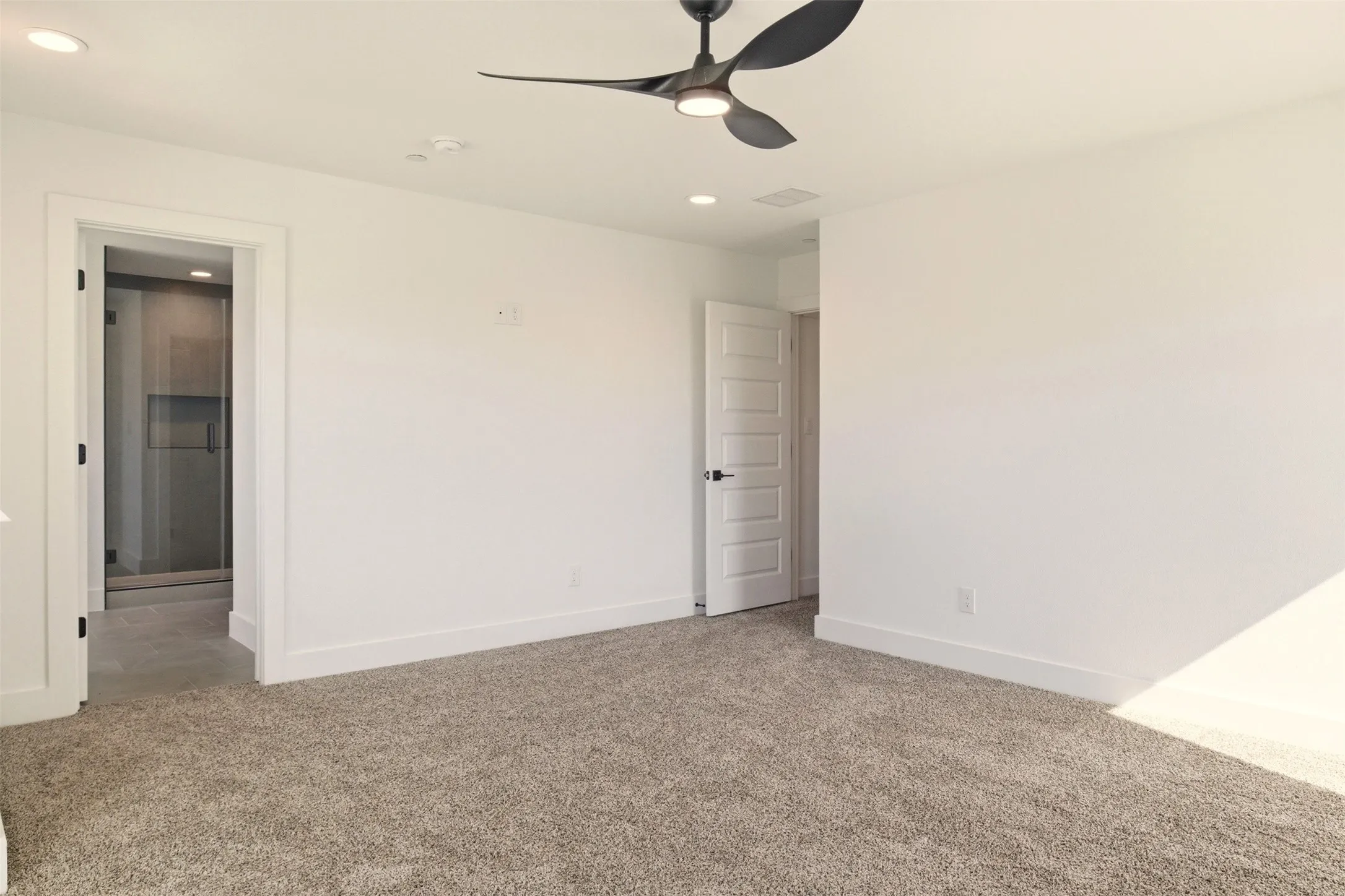 Well-lit room with light-colored carpet flooring, white walls, and a modern ceiling fan