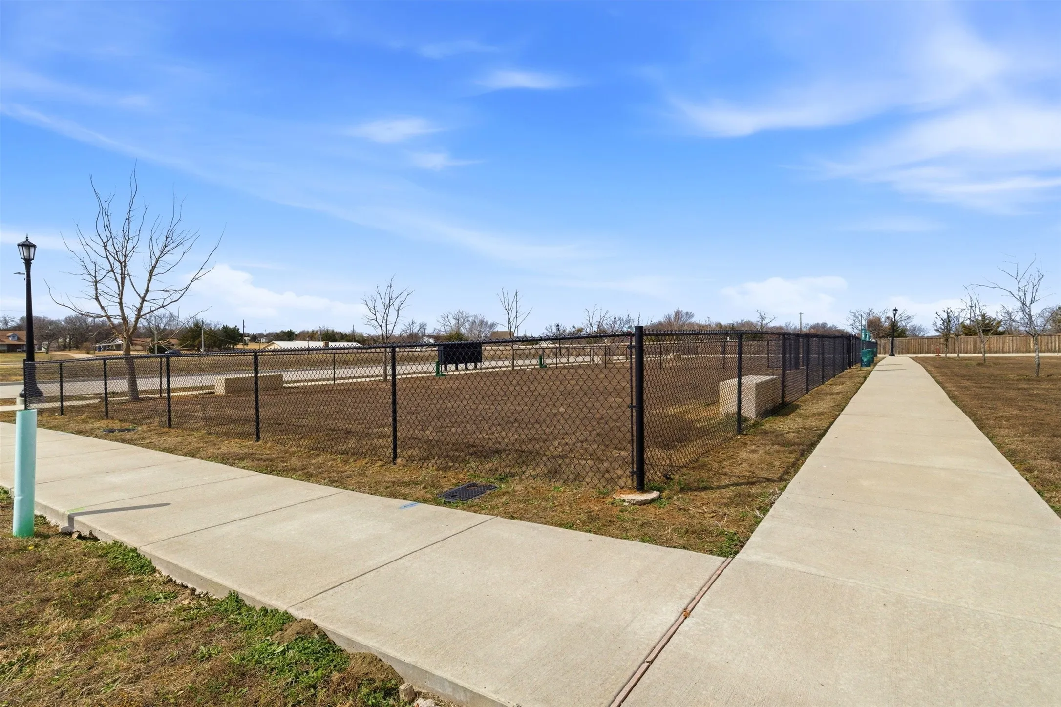 Community amenity featuring a paved walkway, a fenced area, and a streetlamp