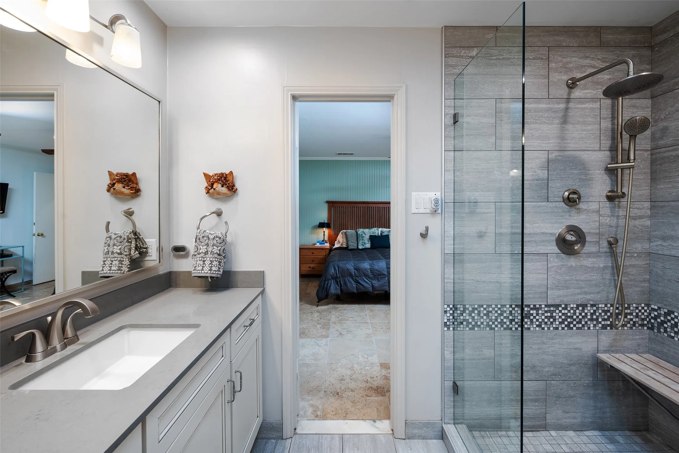 Contemporary bathroom featuring a spacious vanity with a single sink, a large mirror, and a glass-enclosed shower with tile work and a built-in bench