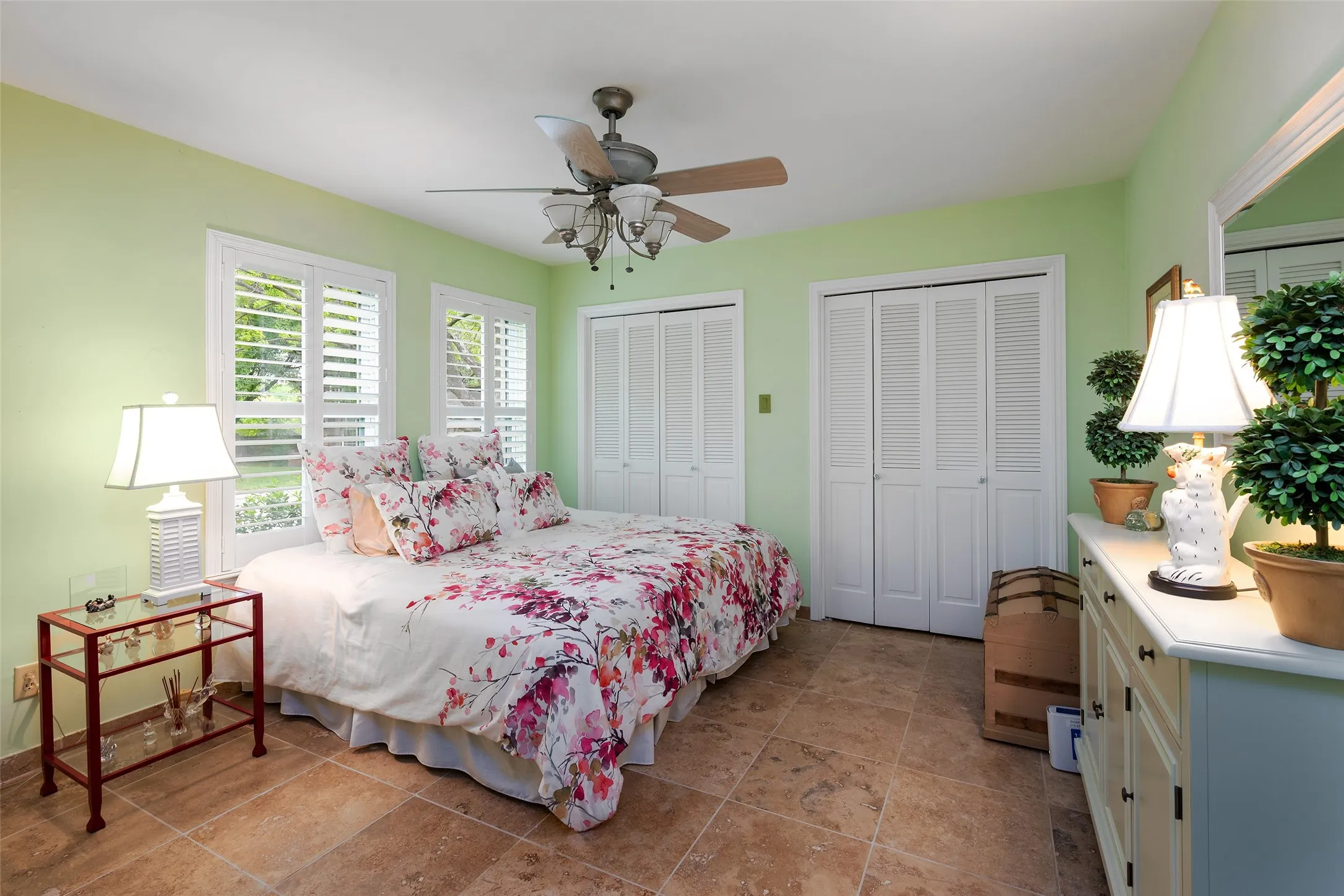 The bedroom features light green walls, two windows with white shutters, and durable terrazzo flooring