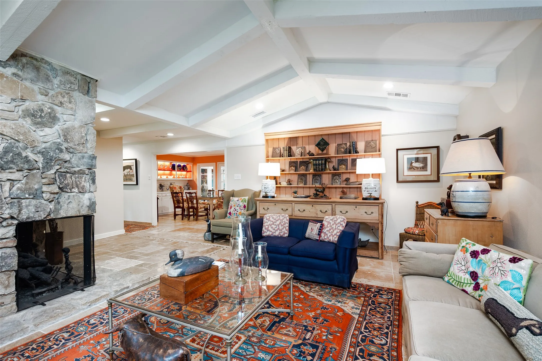 Spacious living area featuring a stone fireplace, vaulted ceilings with exposed beams, and a built-in wooden display cabinet