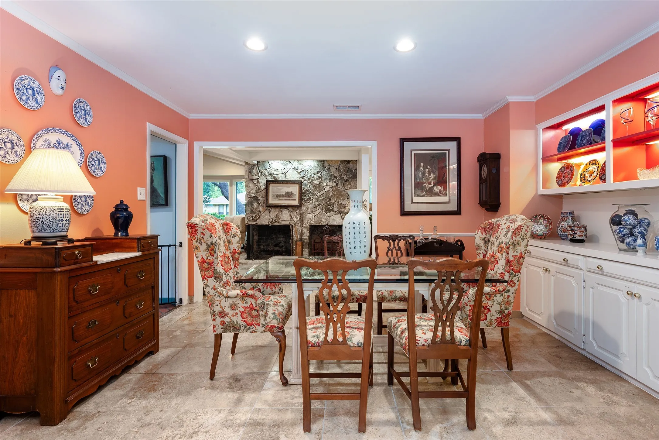 This dining area features light-colored walls, recessed lighting, and a doorway opening into an additional room with a stone fireplace