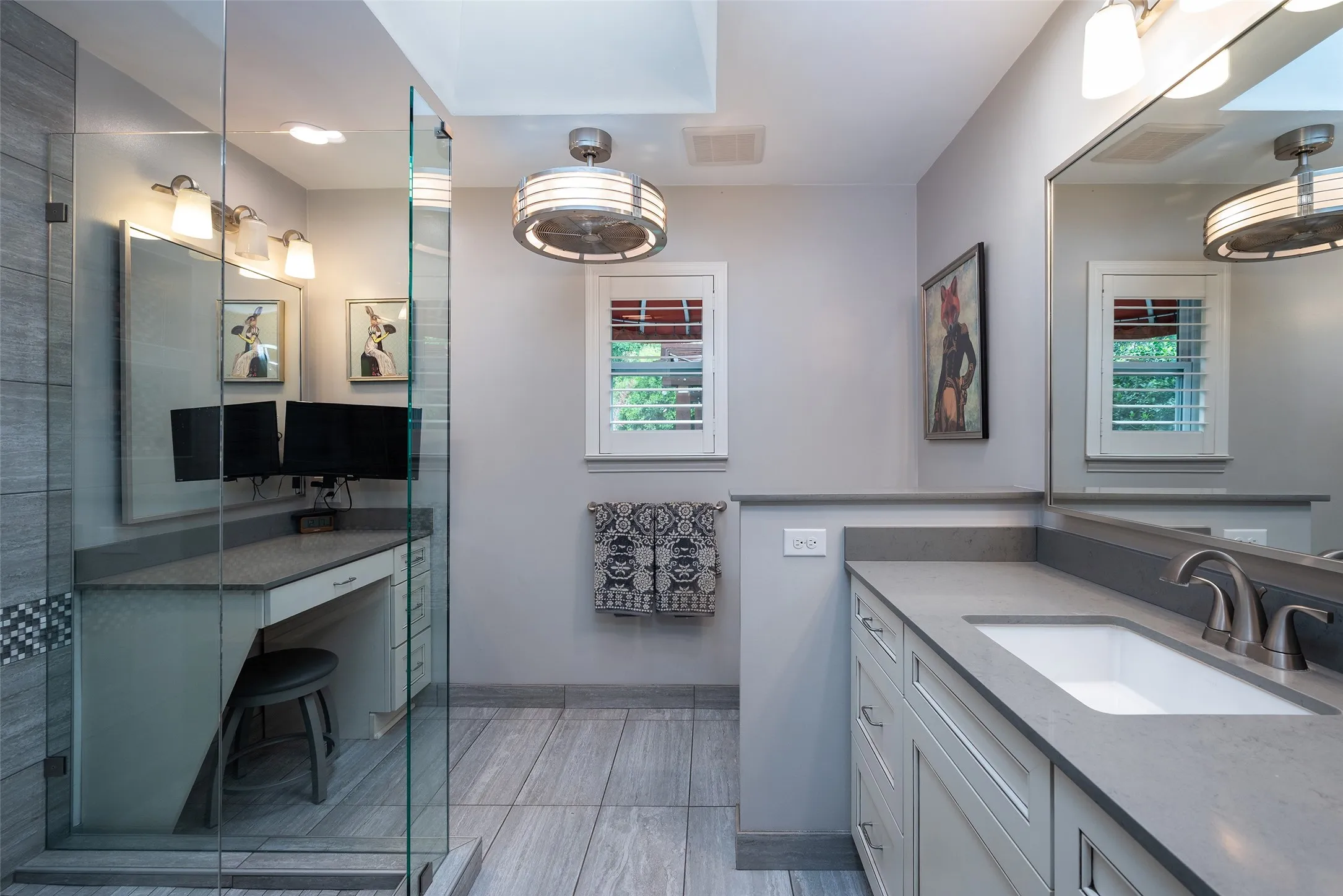 This bathroom features a spacious vanity with an undermount sink and a large mirror, complemented by a separate dressing area with a built-in desk and drawers