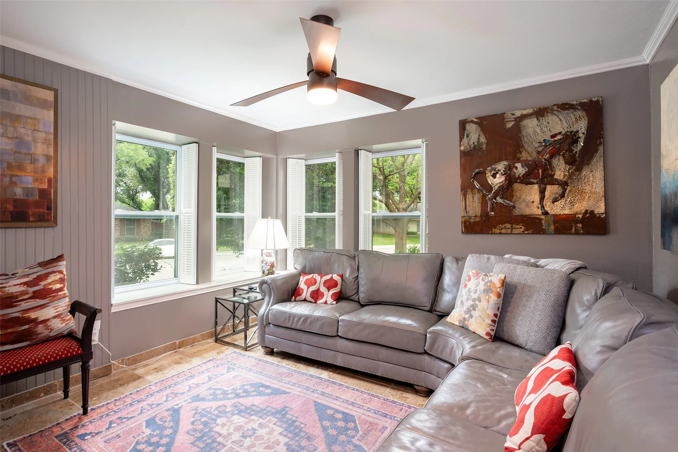 Living area featuring a bay window with white plantation shutters, a ceiling fan, and tiled flooring