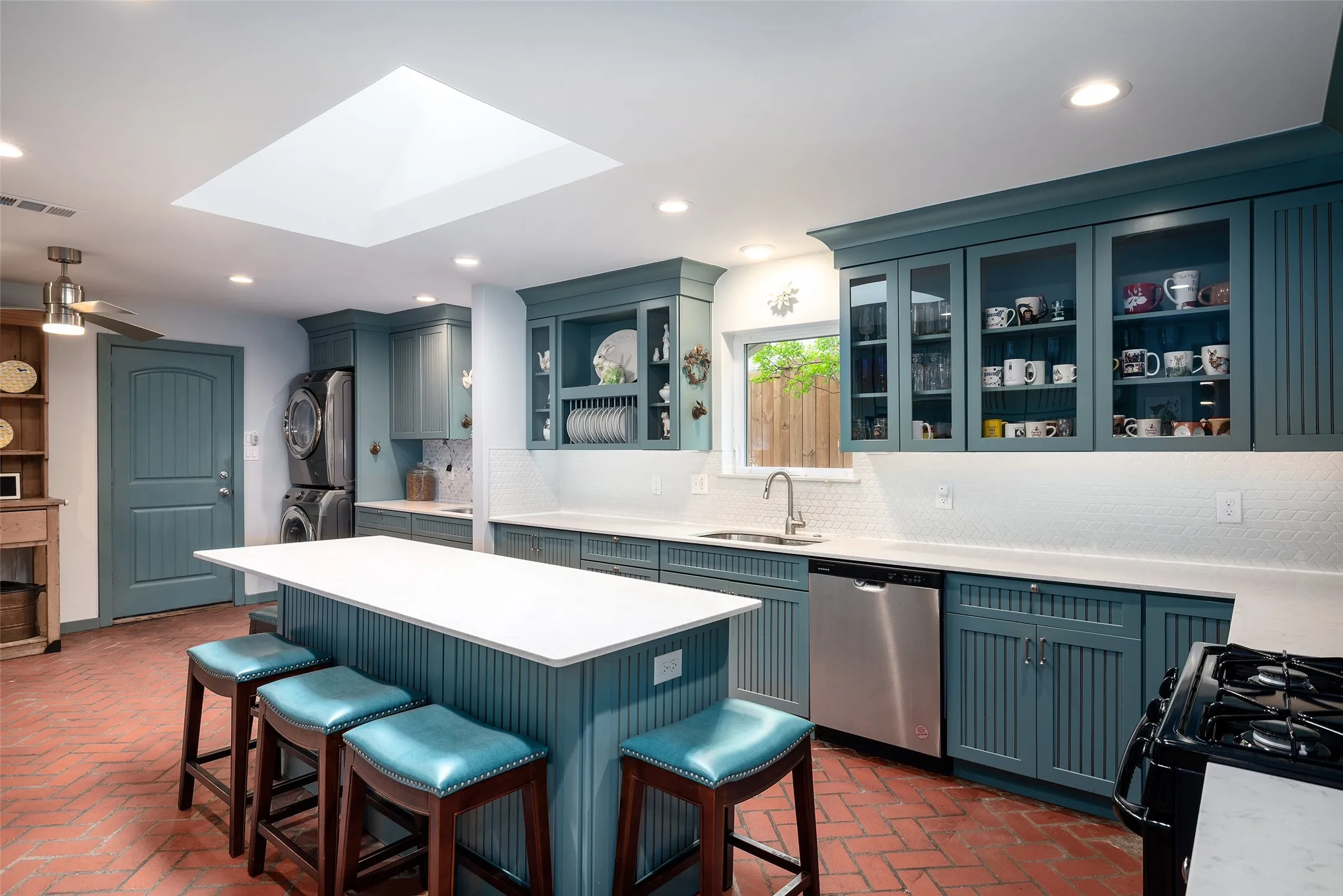 The kitchen features teal cabinetry, a large kitchen island with a white quartz countertop, brick flooring, and a skylight providing natural light