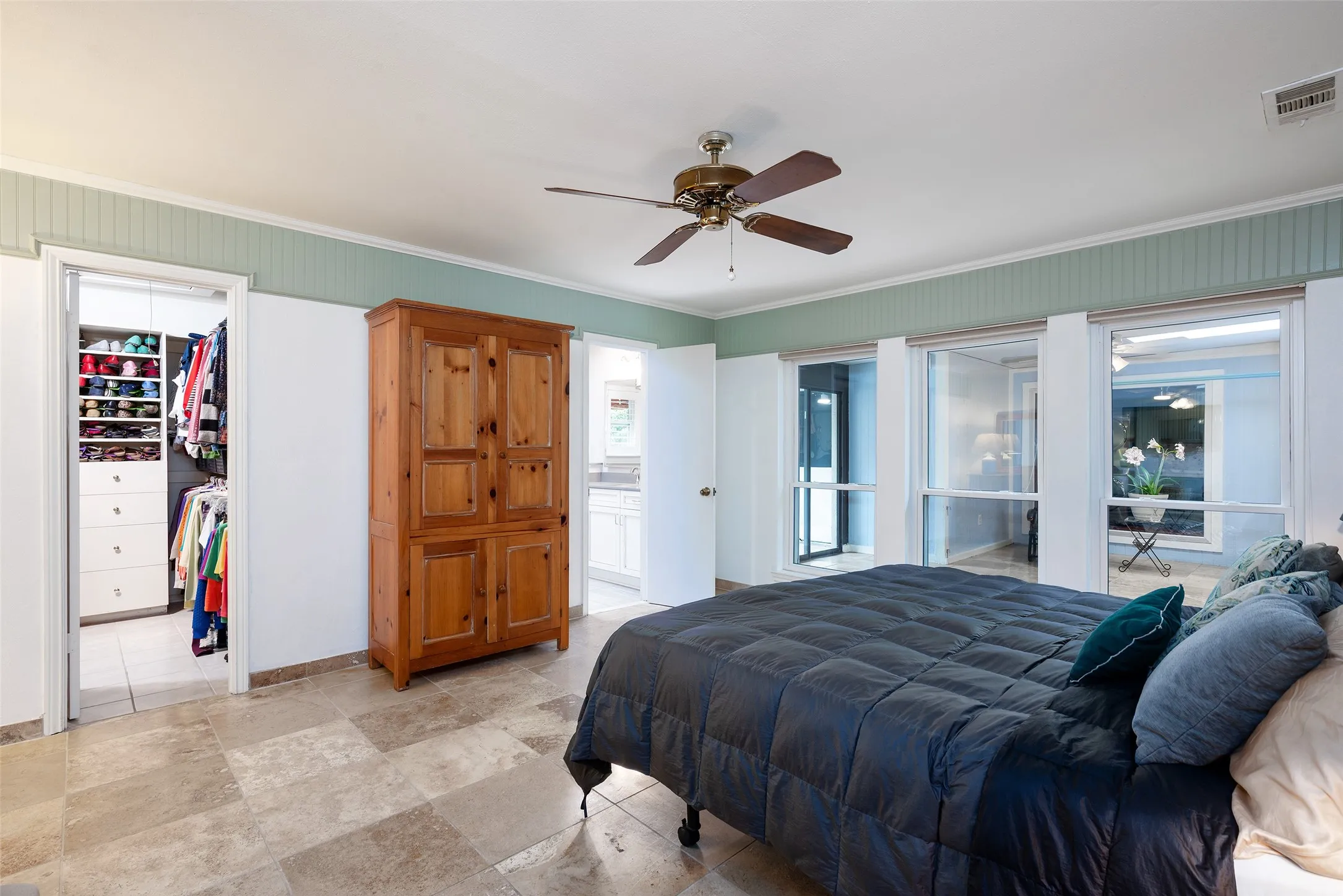 This bedroom features, walk-in closet, large windows providing views of the outdoors, a ceiling fan, and terrazzo flooring