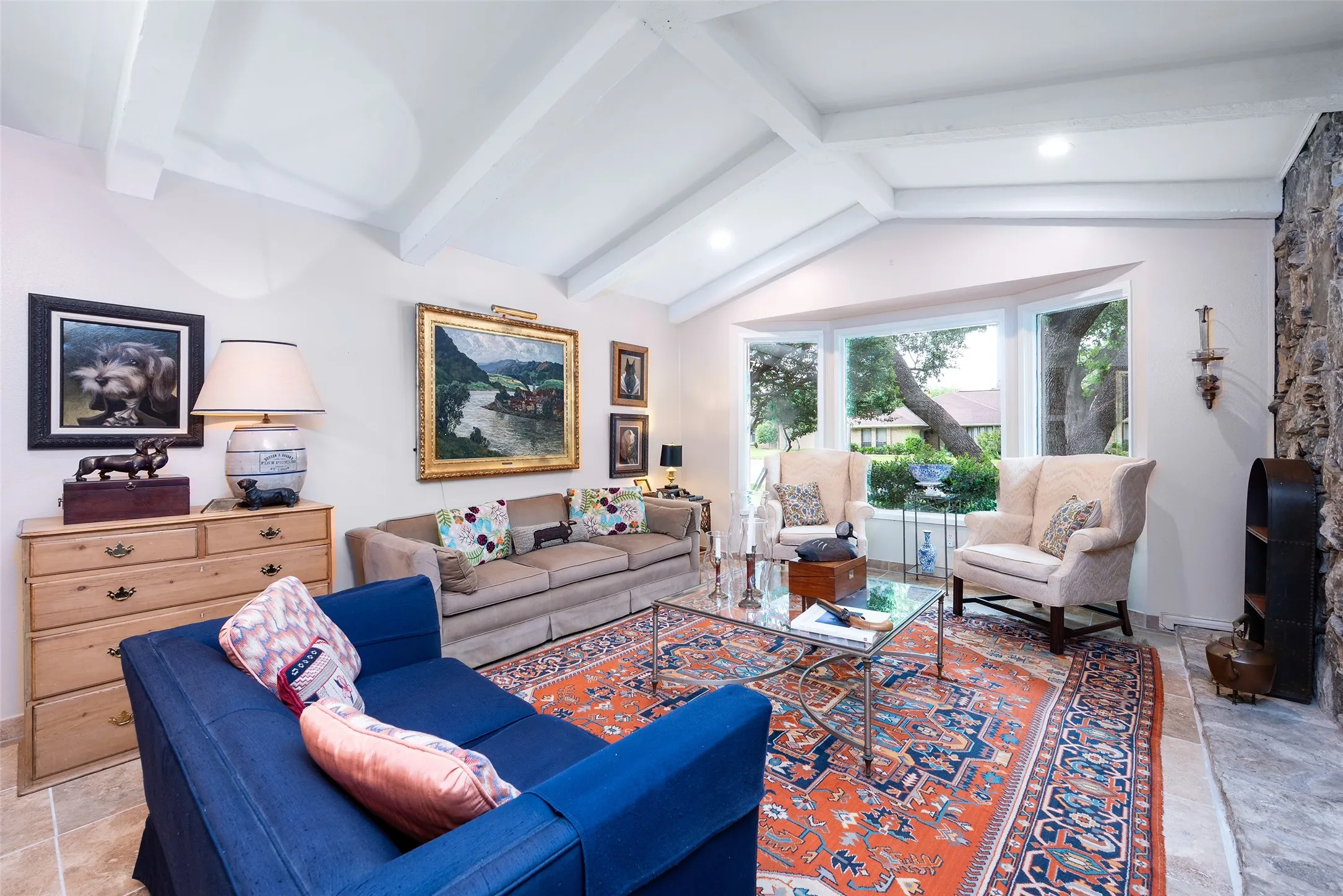 Living area featuring vaulted beamed ceilings, a bay window with views of mature trees, and stone flooring