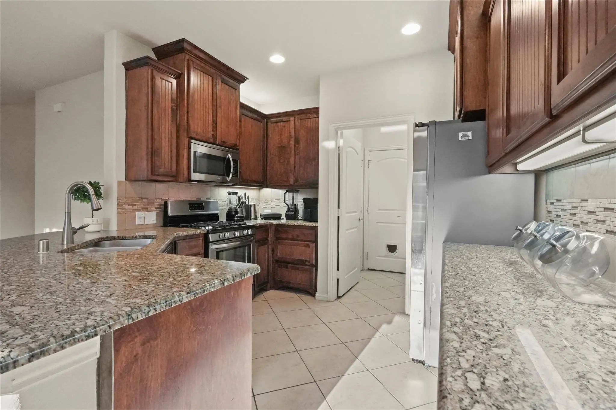 Kitchen featuring light stone countertops, stainless steel appliances, light tile patterned floors, a peninsula, and decorative backsplash
