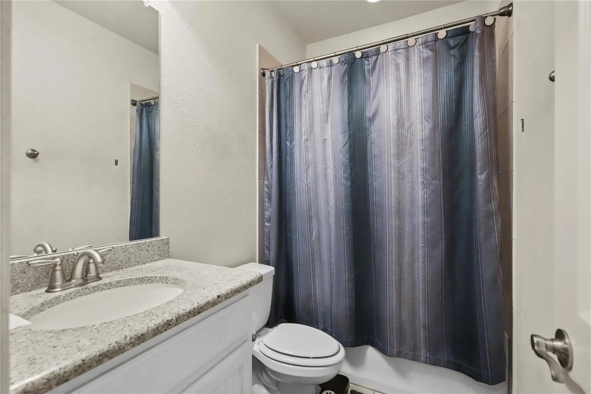 Bathroom featuring vanity, shower / bathtub combination with curtain, and a textured wall