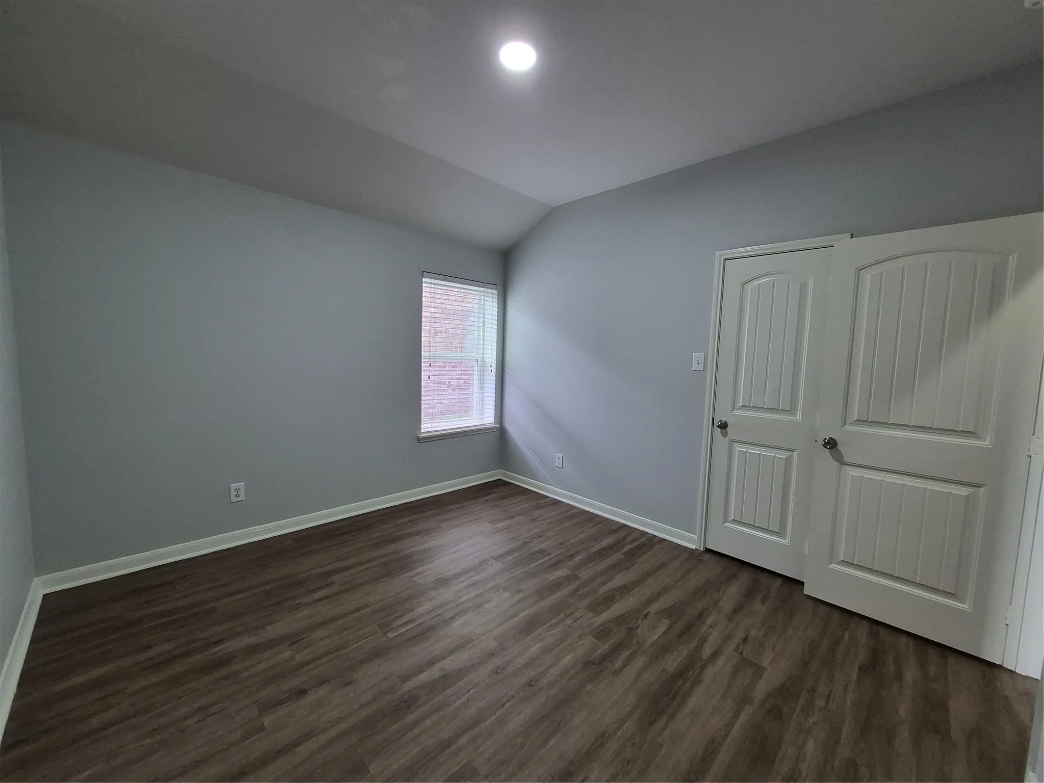 This room features wood-look flooring, light grey walls, and a window with blinds