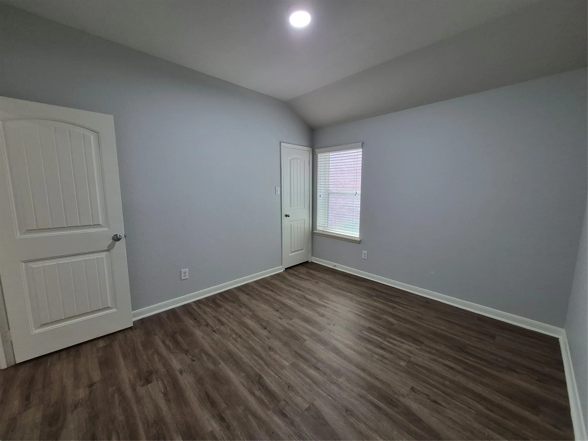 This room features neutral-toned walls, wood-style flooring, a window with blinds, and white trim