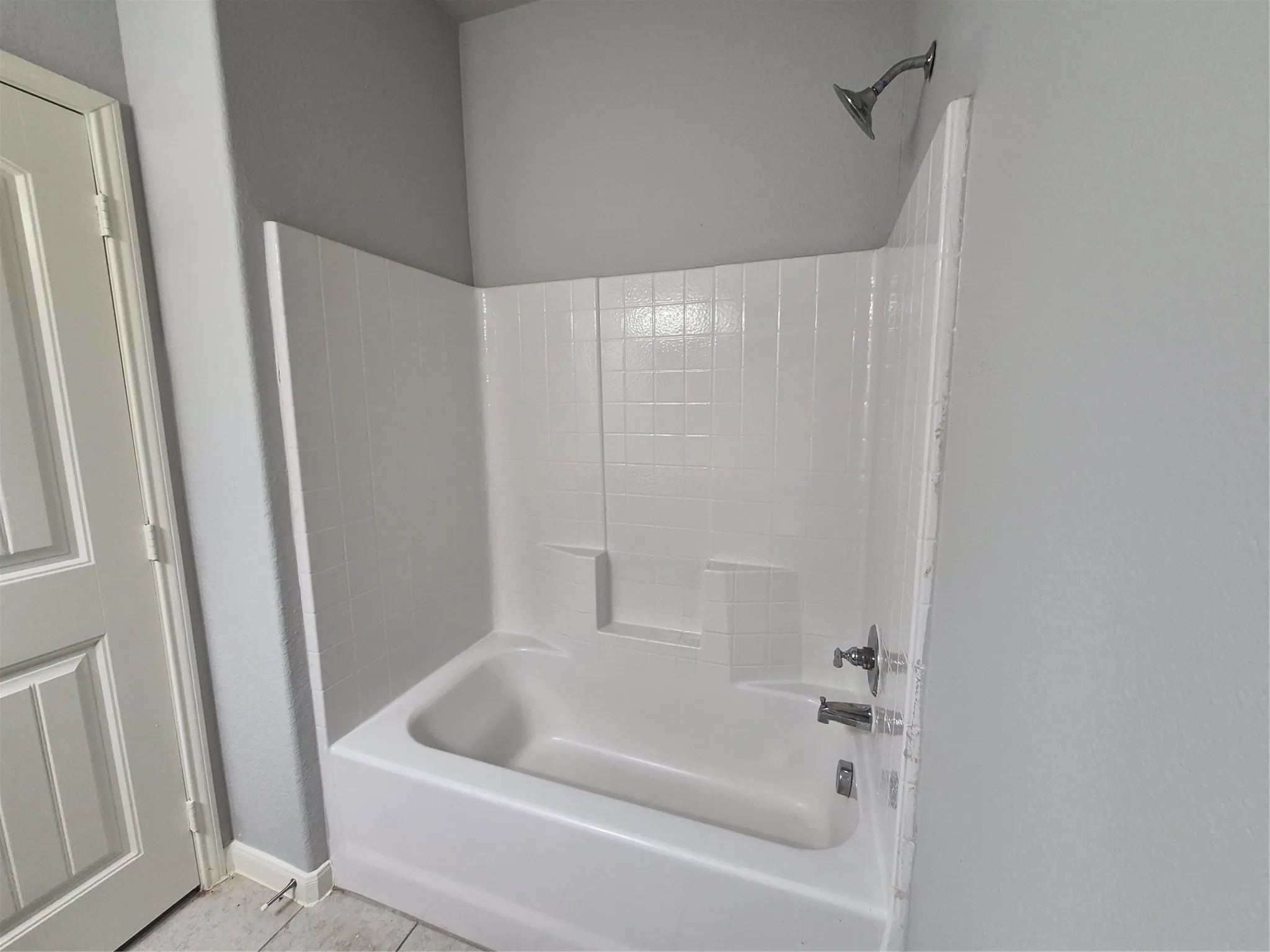The bathroom features a white bathtub with a tiled surround, a chrome showerhead, and a chrome faucet set
