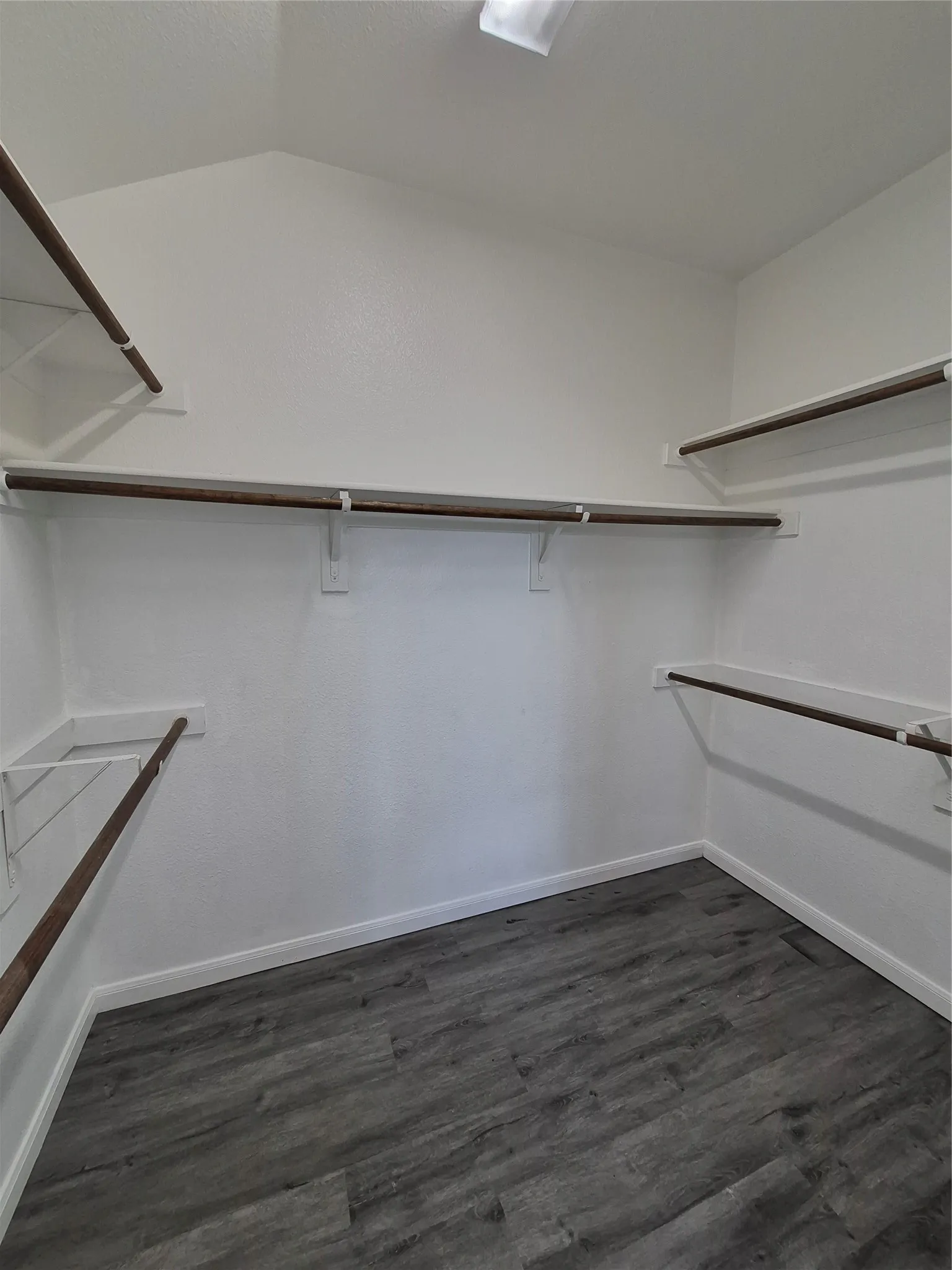 Spacious closet featuring dark-toned flooring and white walls, complete with shelving and hanging rods for ample storage