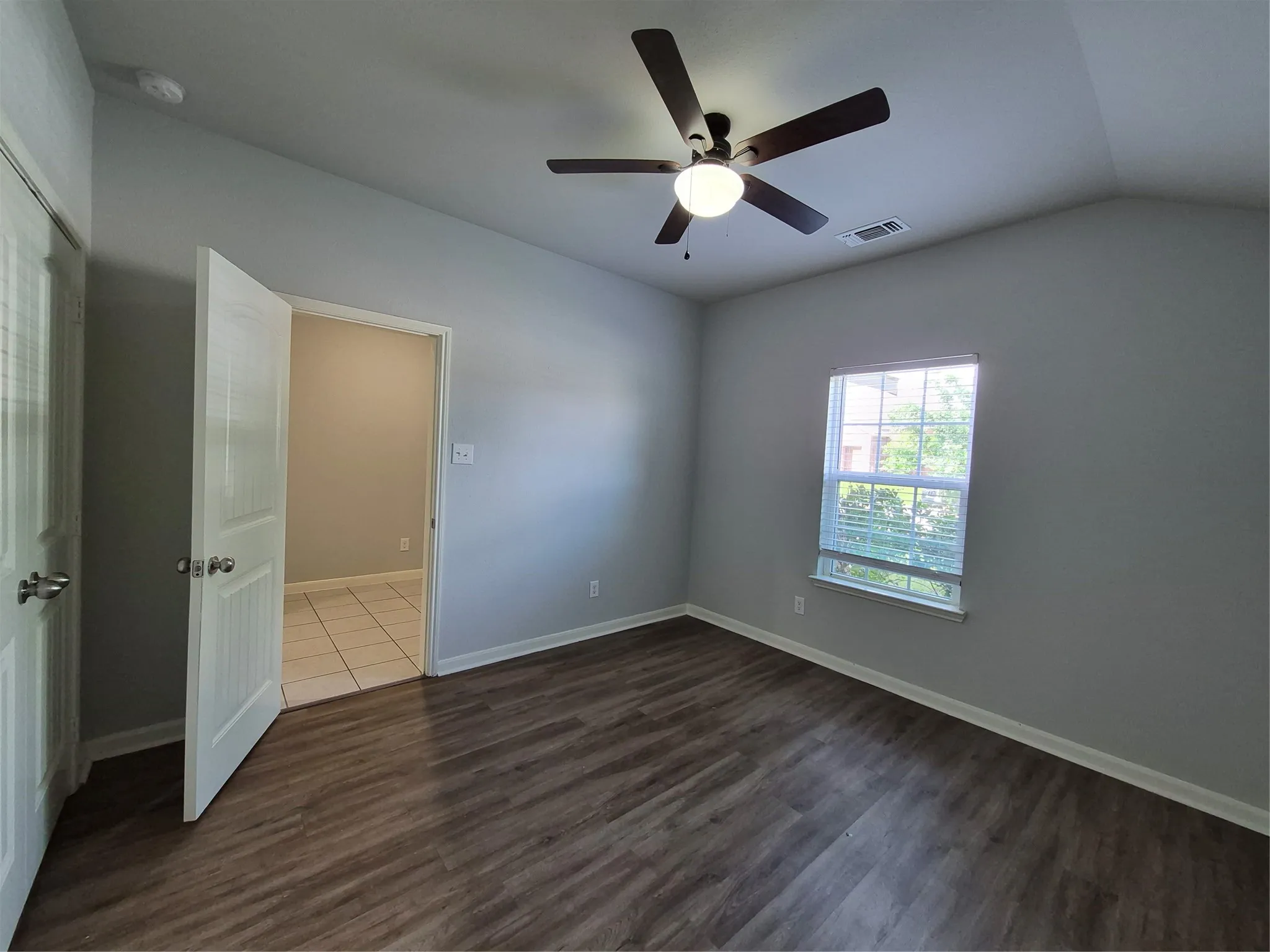 This room features vaulted ceilings, a ceiling fan with integrated lighting, and dark wood-look flooring