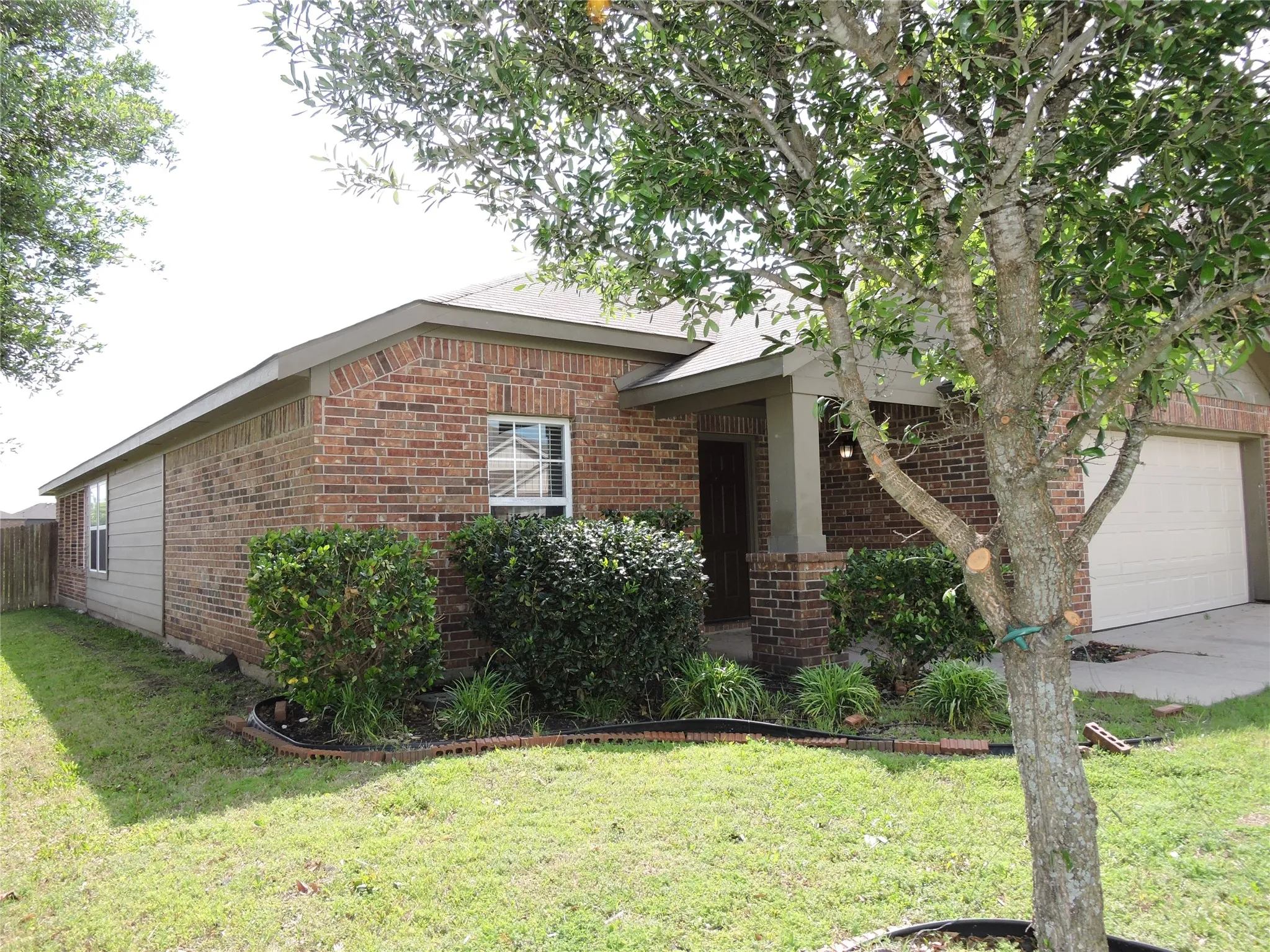 The property features a brick exterior, a covered entryway with columns, an attached garage, a front yard with a lawn, and mature trees
