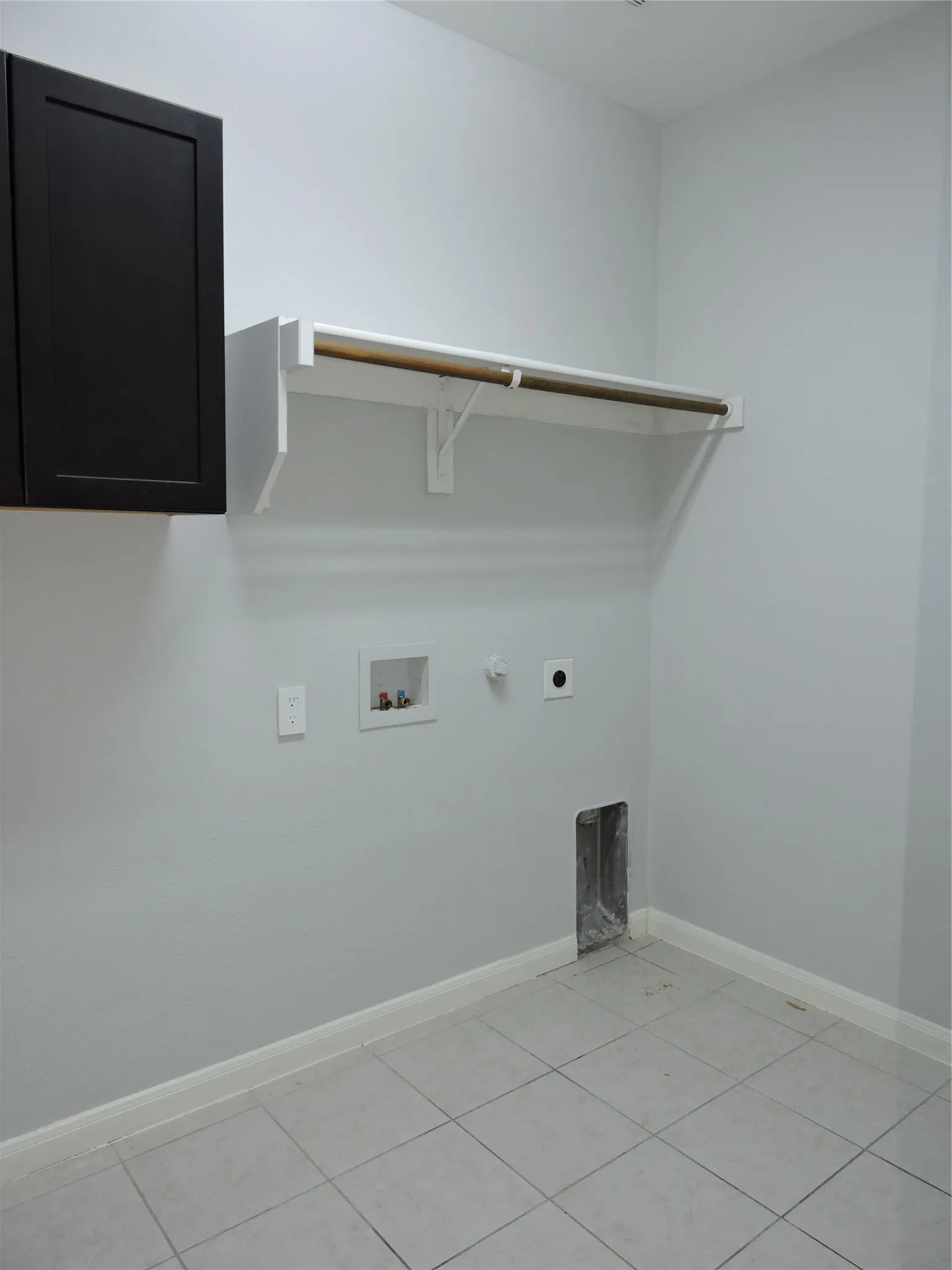 Utility room with tile flooring, a dark cabinet, and a wall-mounted hanging rod