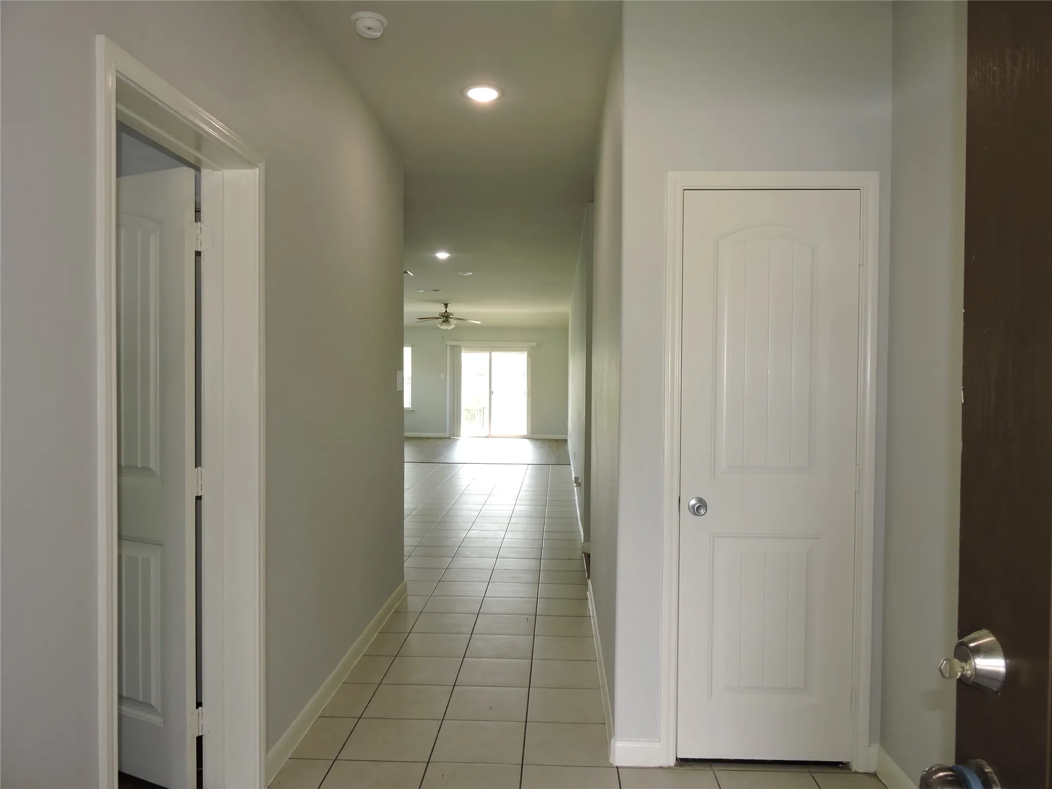 Entryway featuring tiled flooring, a white paneled door, and recessed lighting, leading to an open living area with a ceiling fan and sliding glass doors