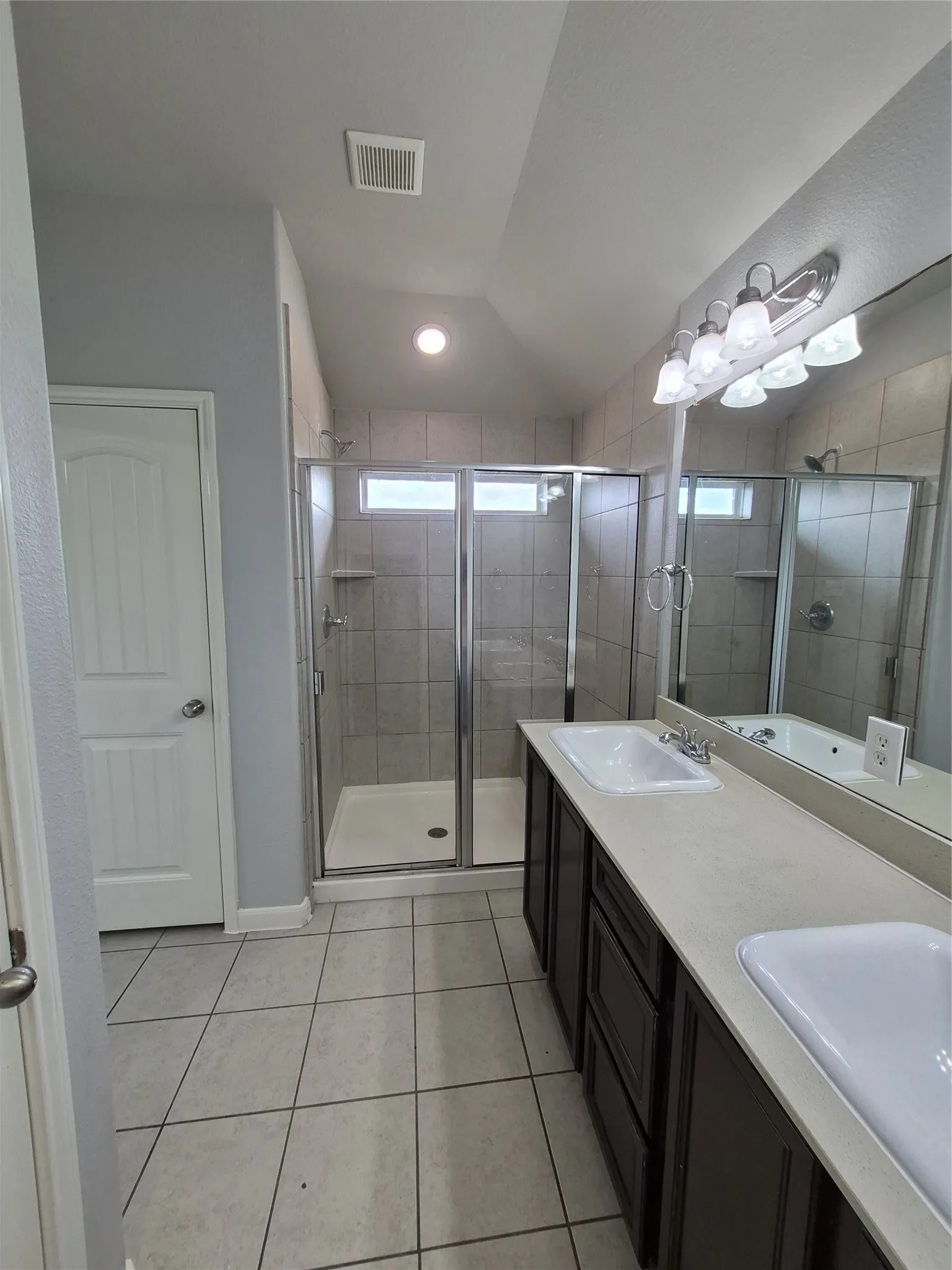 This bathroom features a double vanity with two sinks, a spacious shower with a glass enclosure, and tile flooring