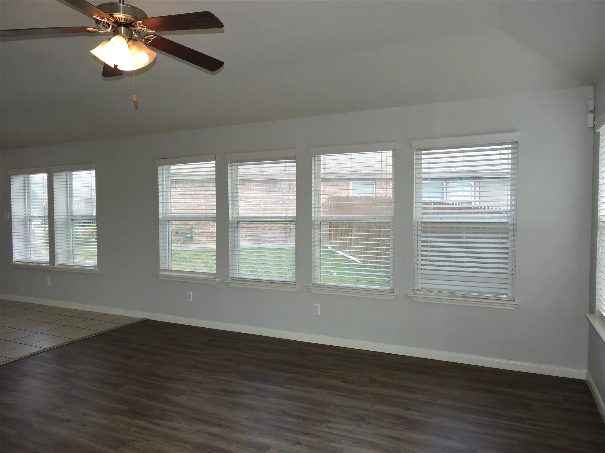 Living area featuring wood-look flooring, multiple windows with blinds, and a ceiling fan with integrated lighting