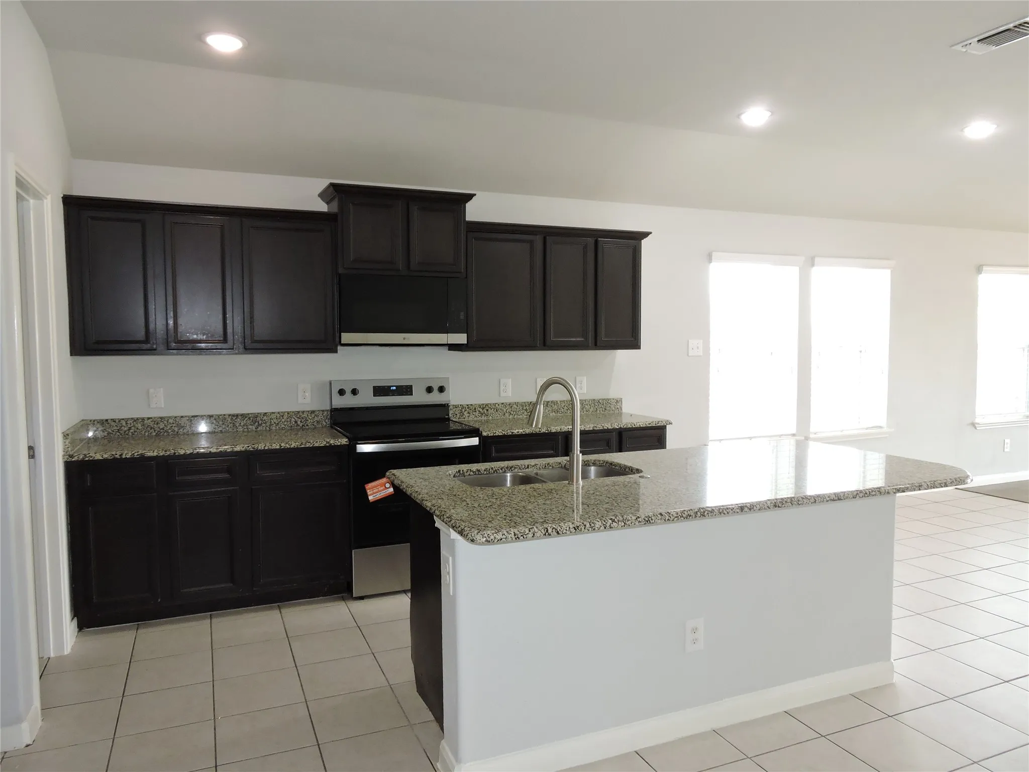 The kitchen features dark cabinetry, speckled countertops, a stainless steel sink, and an electric range with an overhead microwave