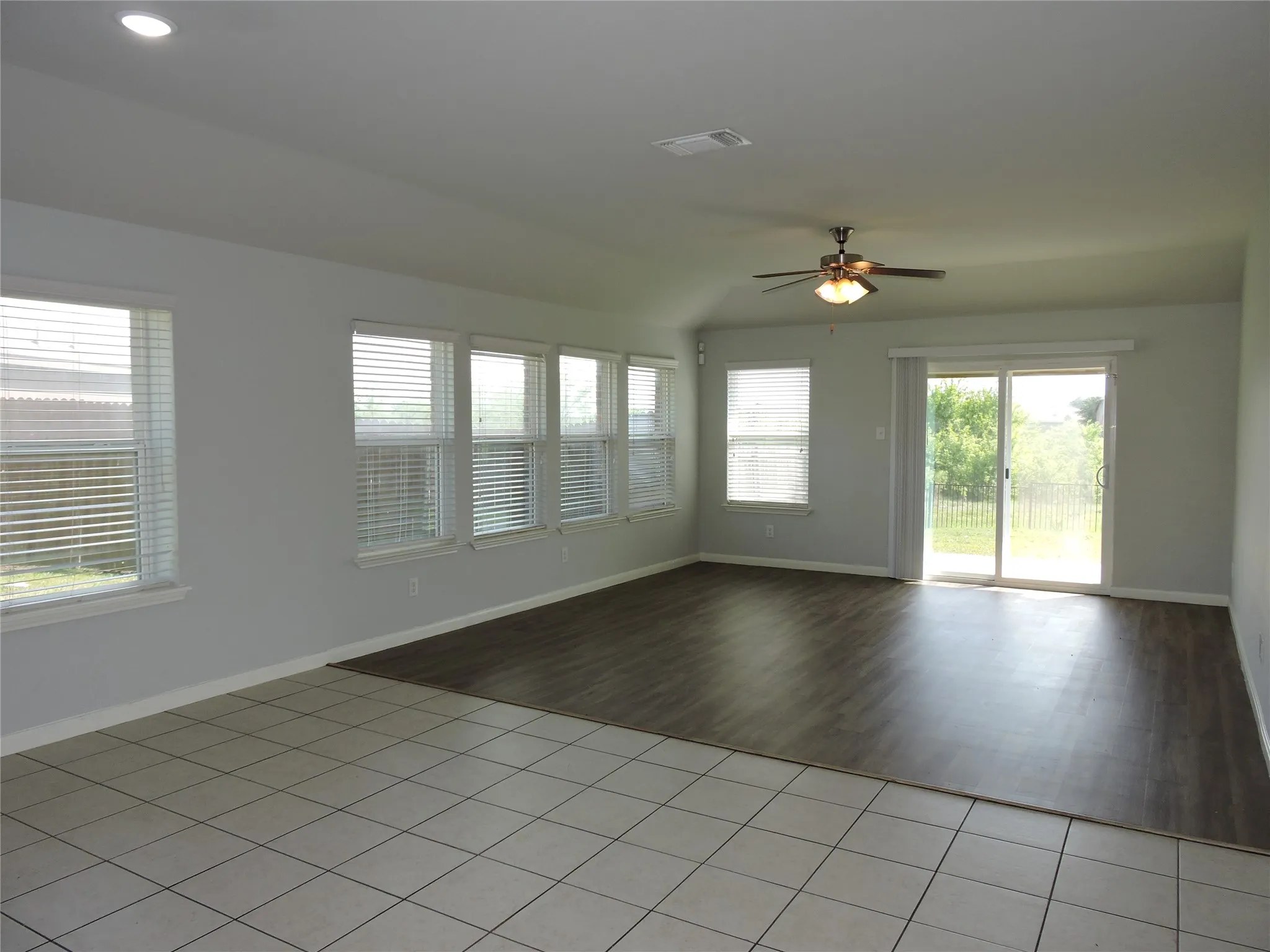 Spacious room featuring a combination of tiled and wood-look flooring, a ceiling fan, recessed lighting, and ample natural light from multiple windows and a sliding glass door