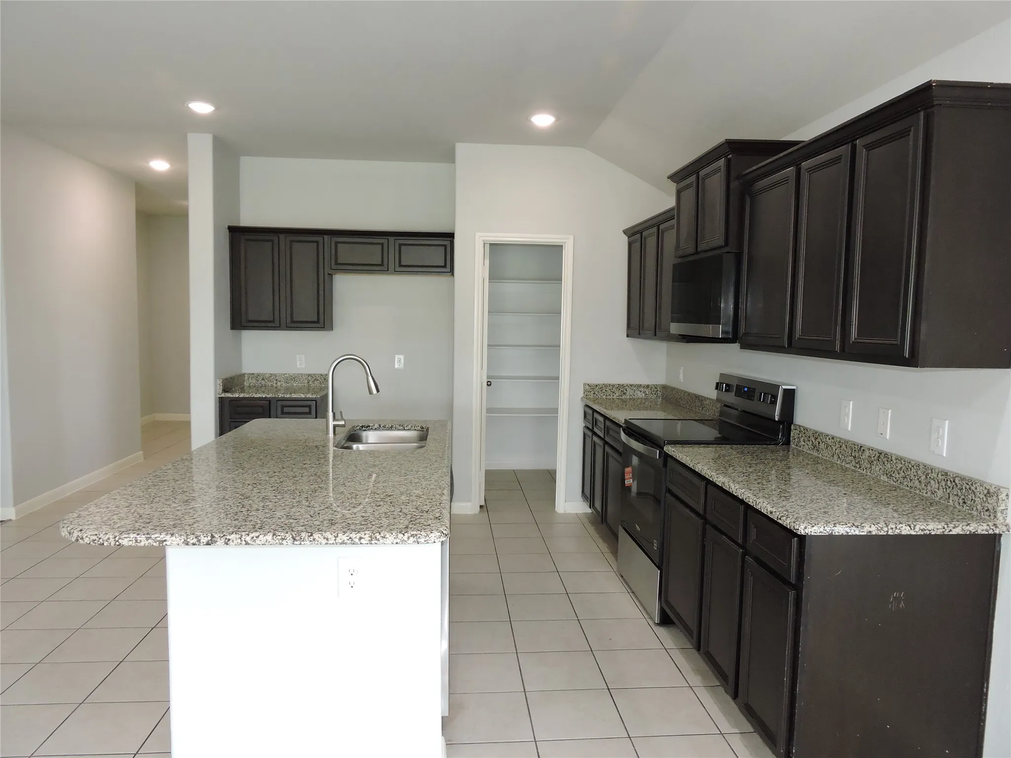The kitchen features dark wood cabinetry, granite countertops, stainless steel appliances, and a central island with an integrated sink