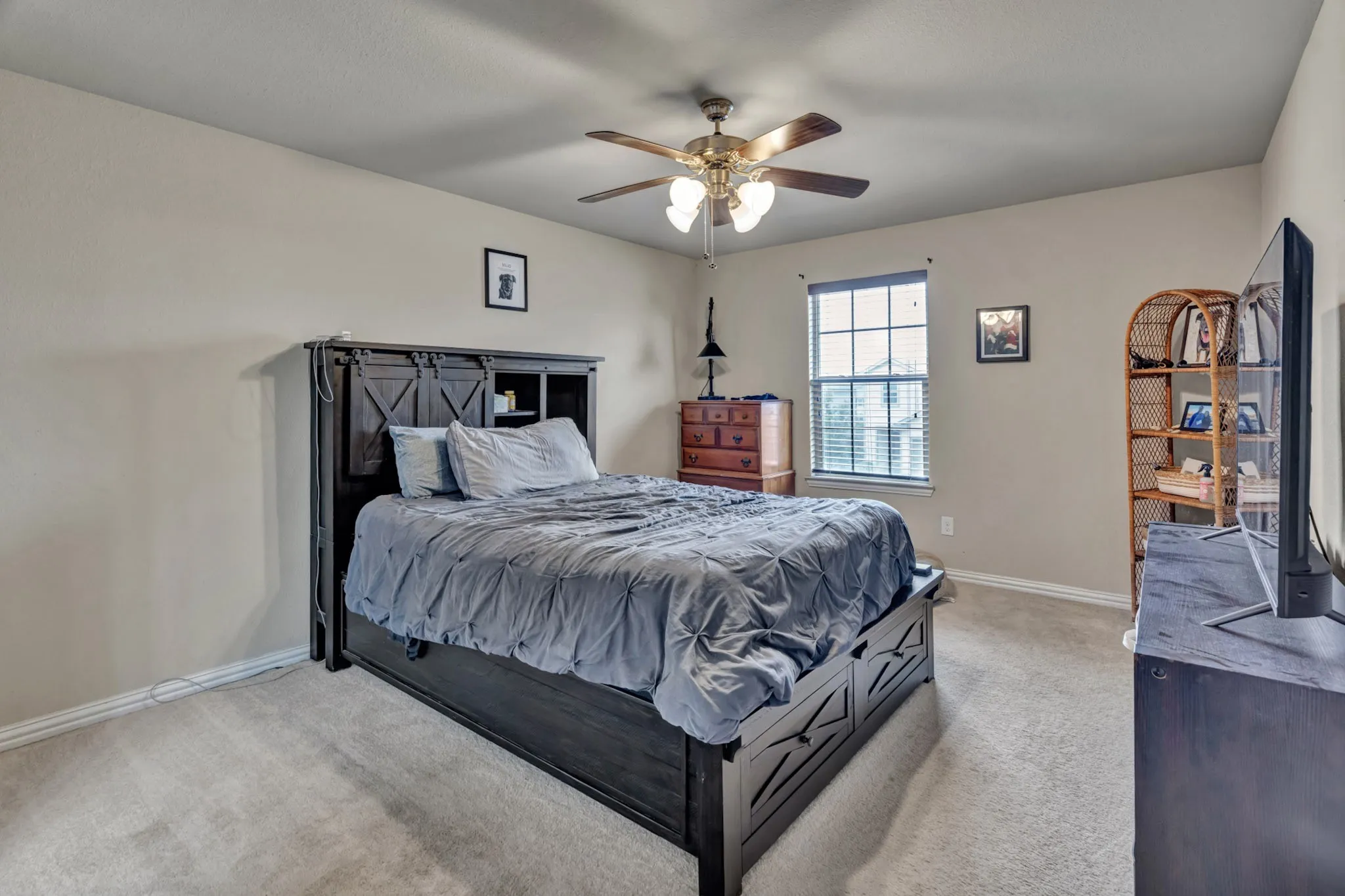 This bedroom features light-colored walls, carpeted flooring, and a ceiling fan with integrated lighting