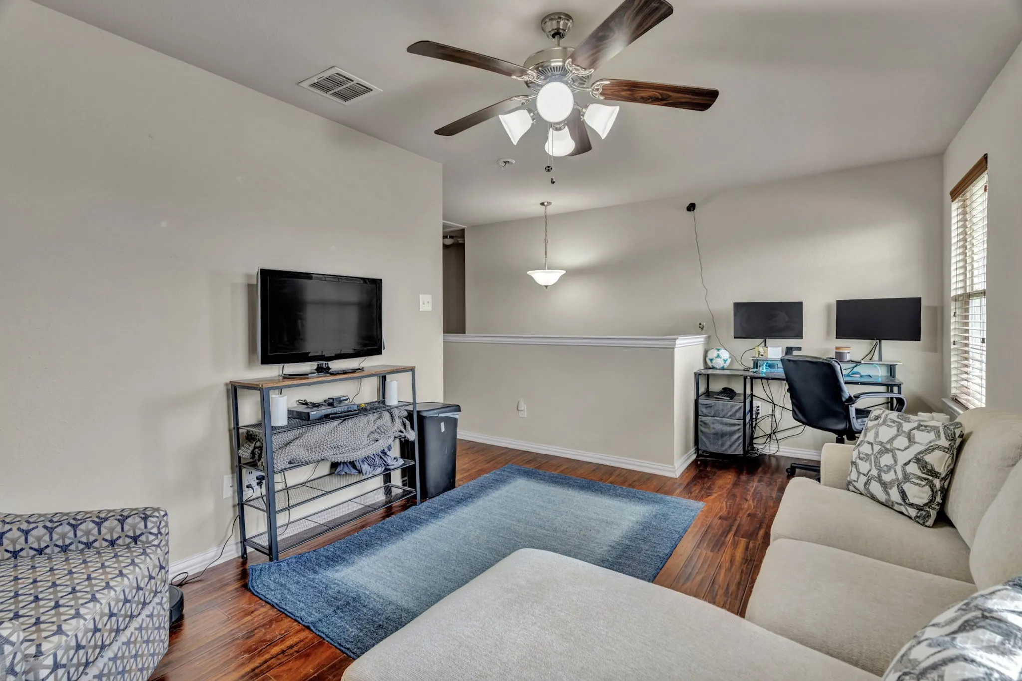 Living area with hardwood flooring, a ceiling fan with integrated lighting, and window blinds
