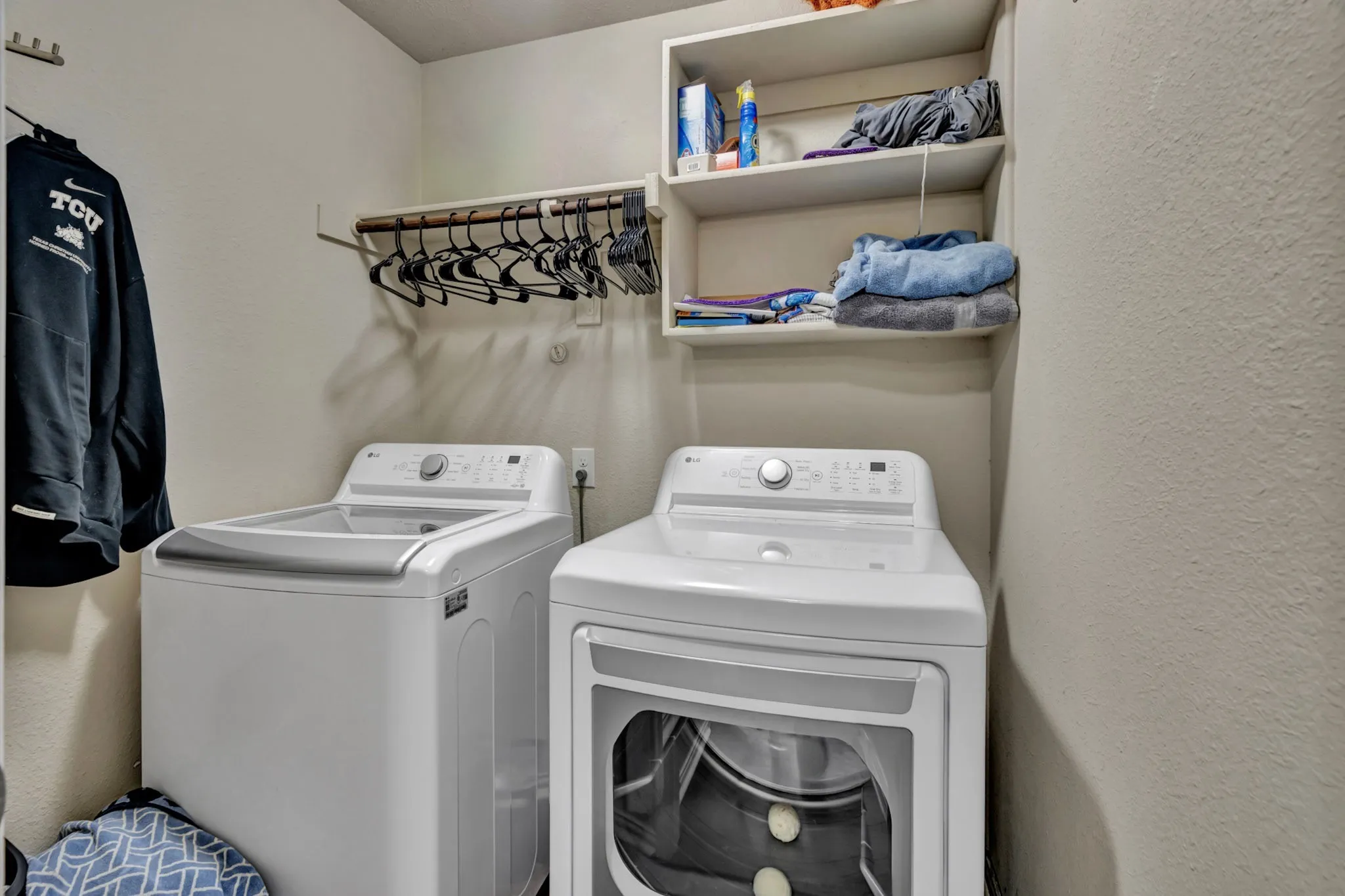 Dedicated utility area featuring a washer and dryer, an overhead shelving unit, and a clothes hanging rod