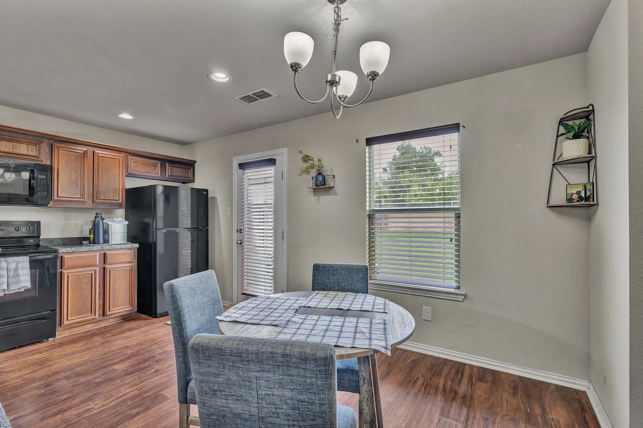 This kitchen and dining area features rich wood cabinetry, black appliances, and durable wood-look flooring