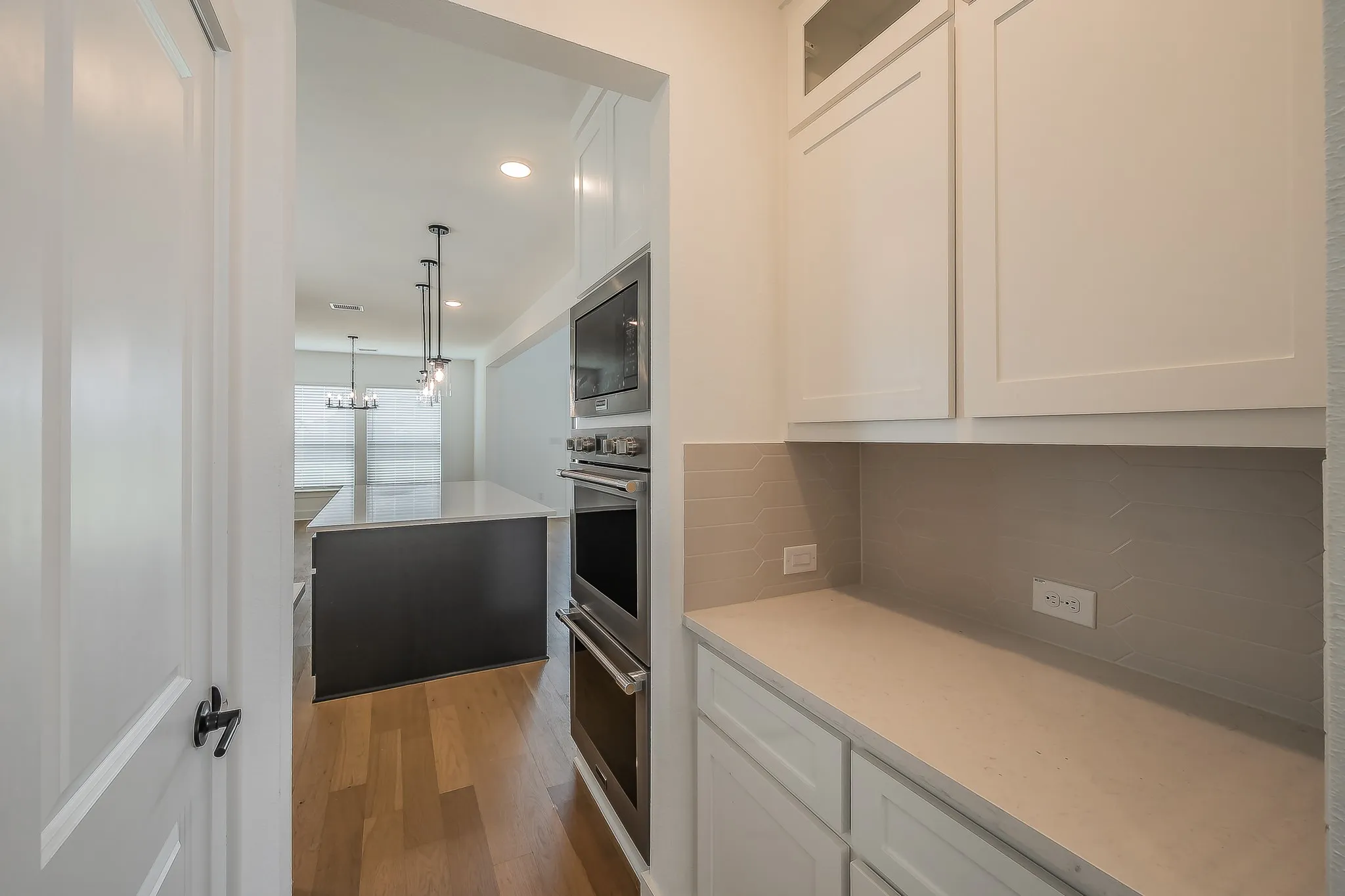 The kitchen features light wood flooring, a dark kitchen island with a light countertop, and pendant lighting