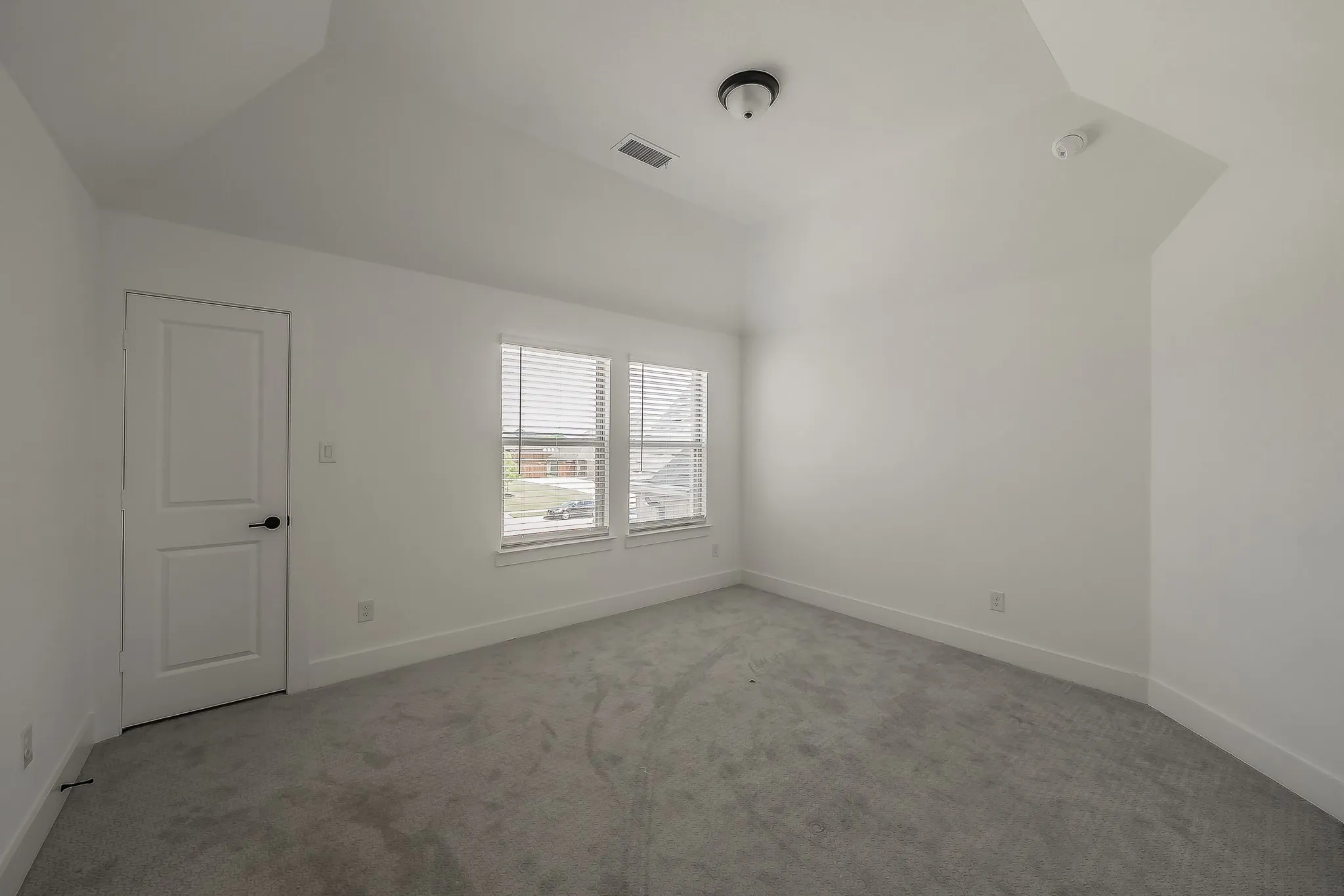 This room features light gray carpeting, white walls, and a vaulted ceiling