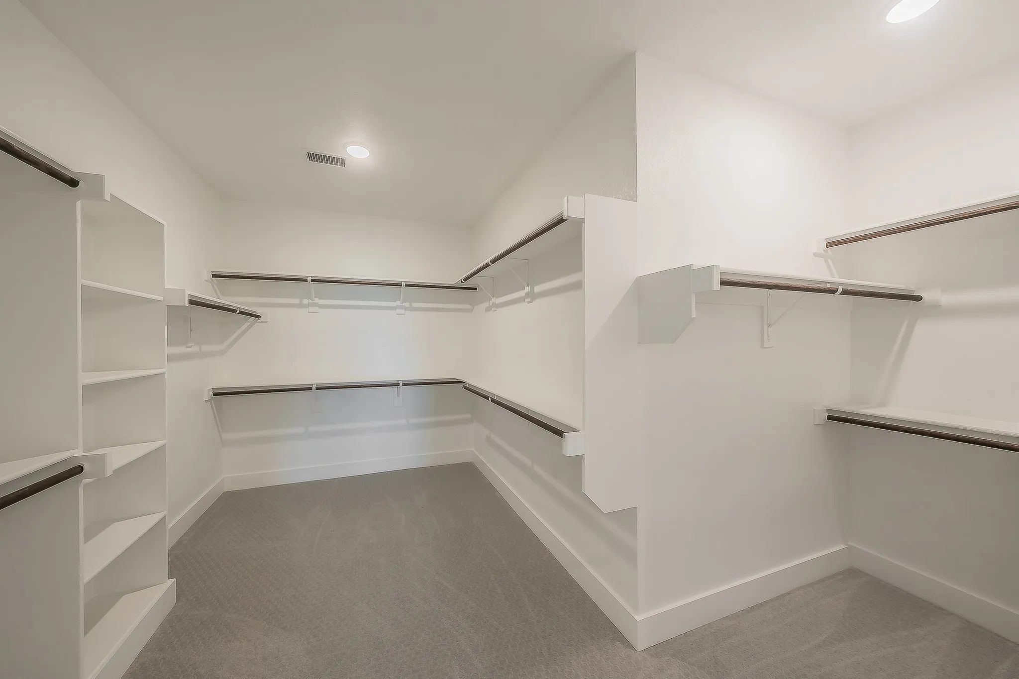 Spacious walk-in closet featuring white built-in shelving, hanging rods, and carpeting